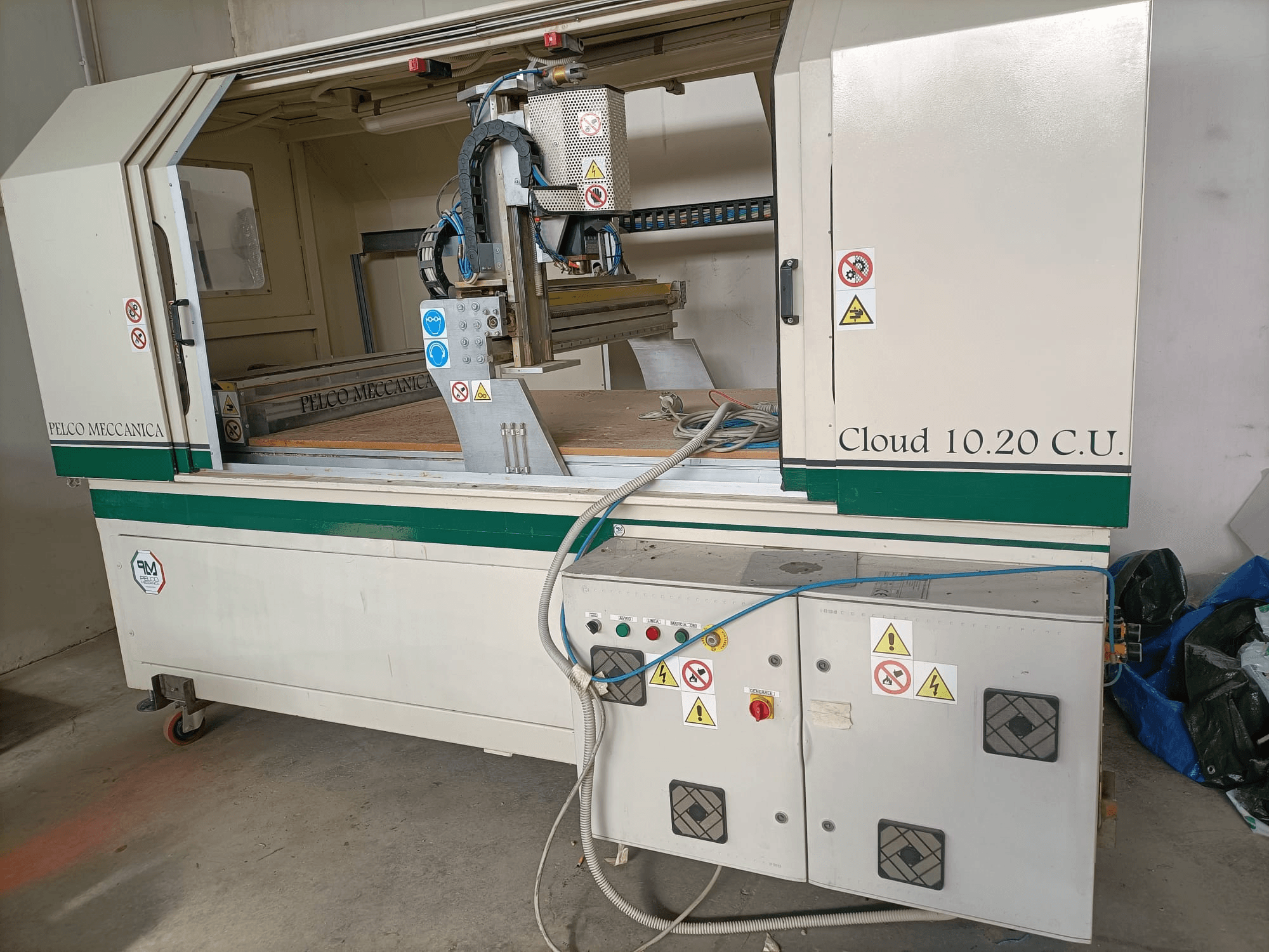 CNC router MECCANICA CLOUD 10.20 C.U., kontrol paneli ve çalışma alanını gösteren önden görünüm, güvenlik etiketleri ve hortumlar görünür.