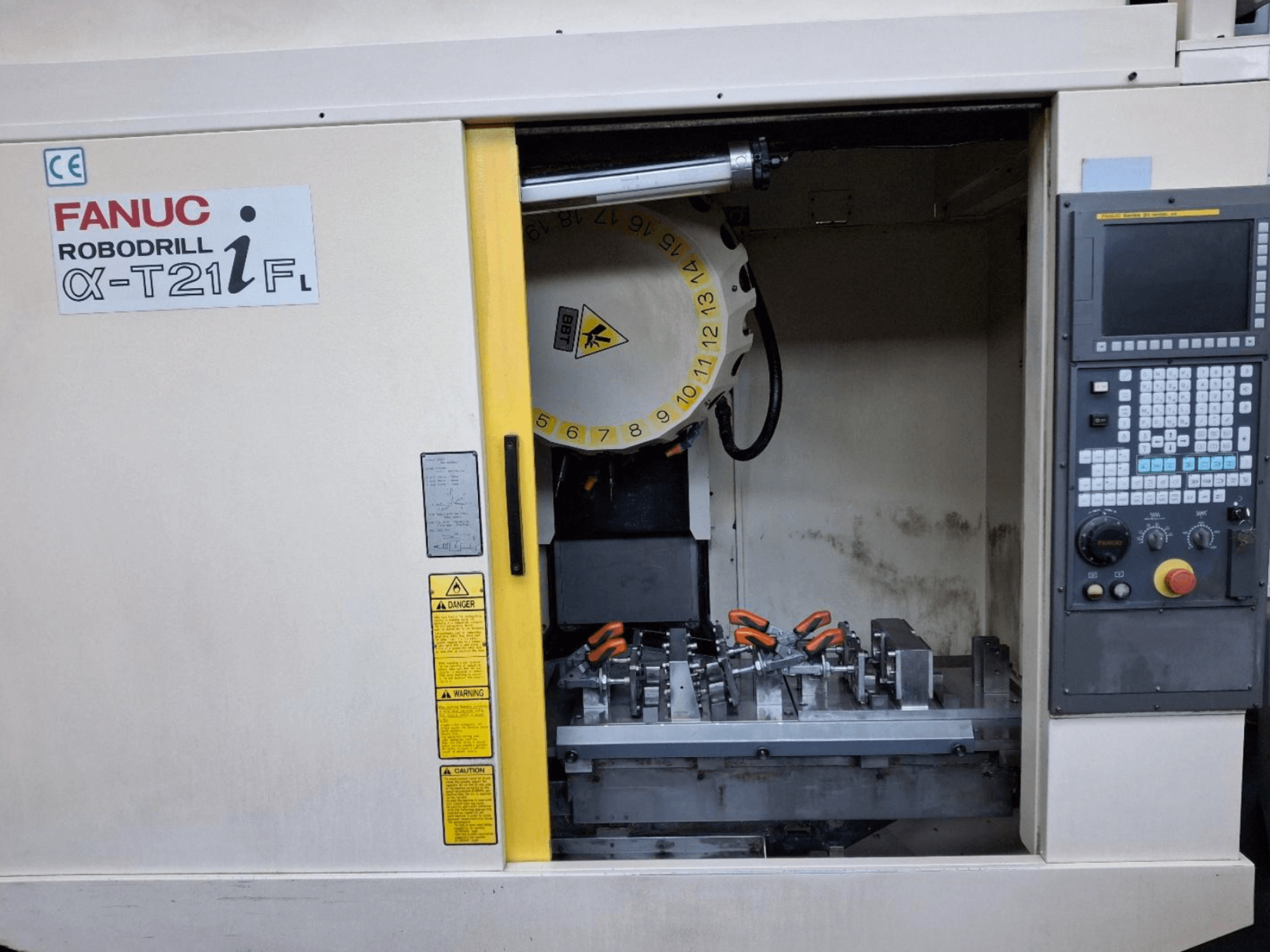 FANUC ROBODRILL α-T21iFL dikey işleme merkezinin önden görünümü, makine kabini içindeki aletleri ve kontrolleri gösterir.