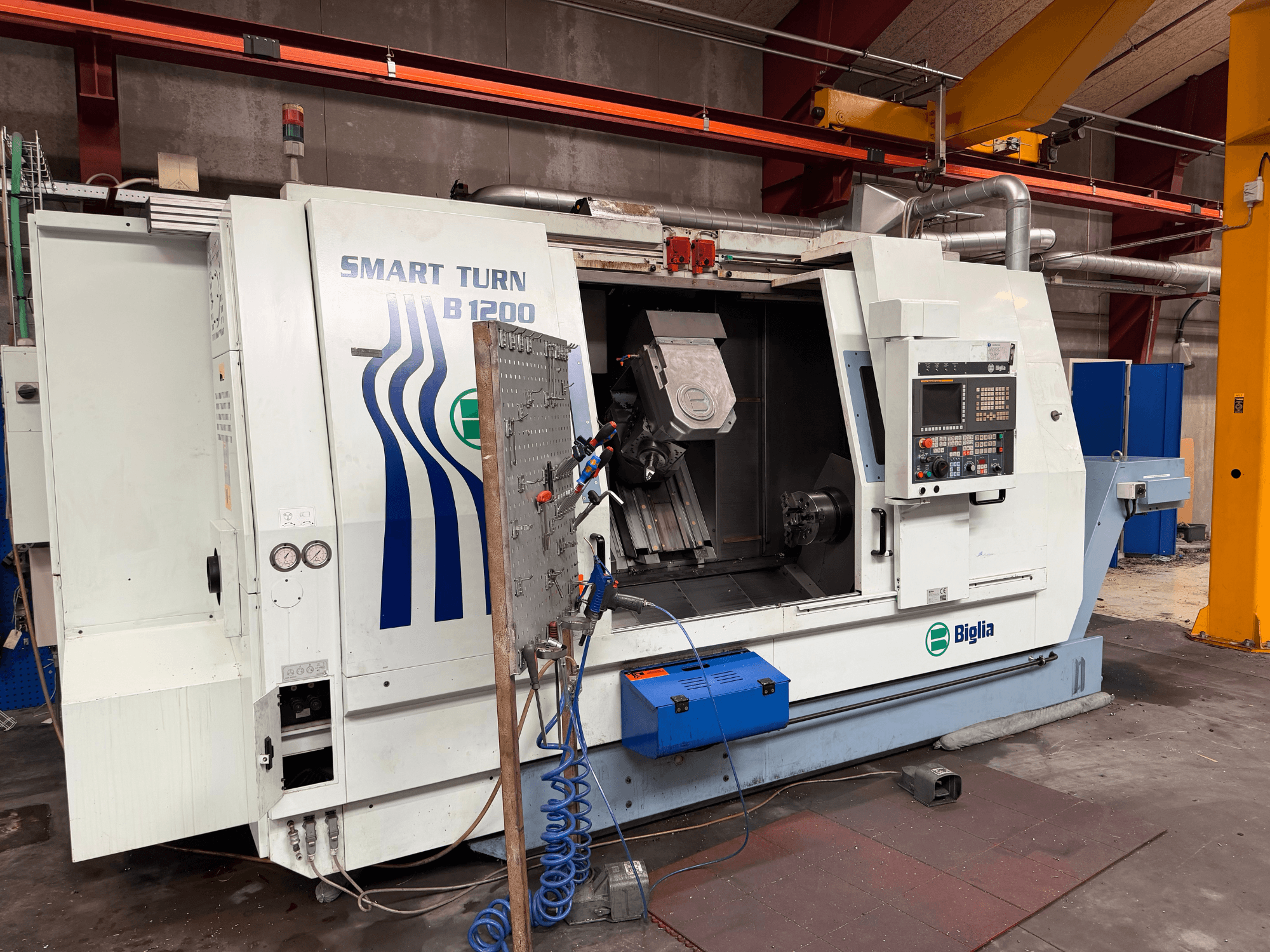 Biglia B.1200/S-Smart tornalama-frezeleme merkezinin önden görünümü; kontrol paneli, iş milinde bulunan bir iş parçası ve basınç göstergeleri görülmektedir.