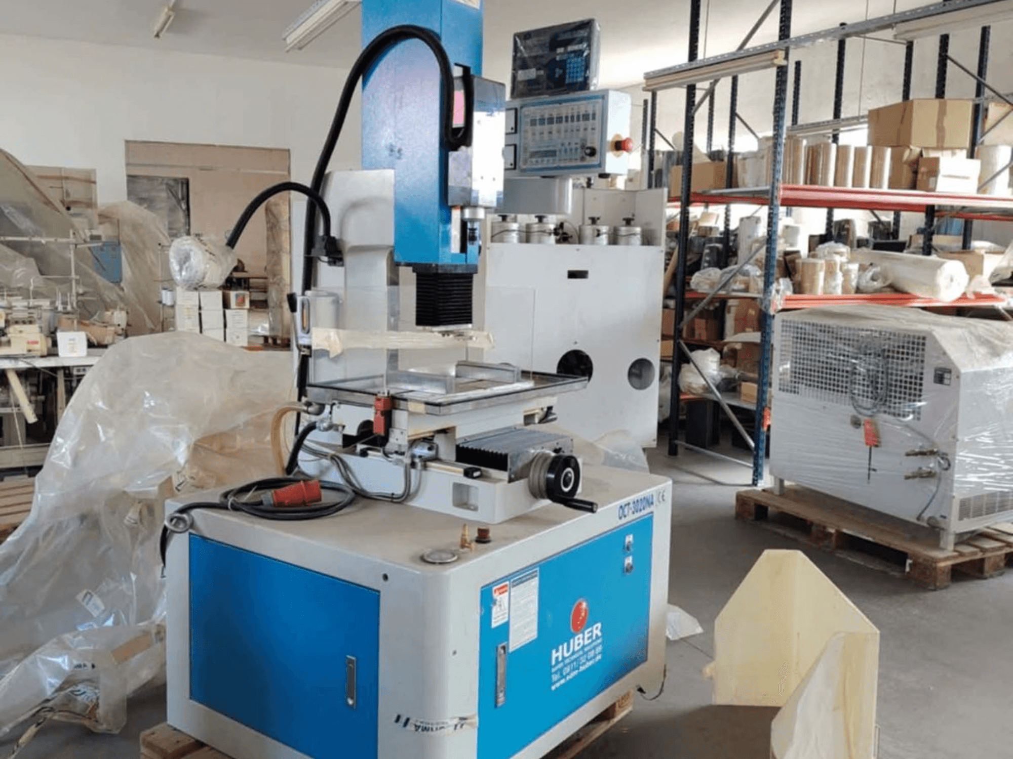 Bir atölyedeki HUBER OCT-3020 NA kalıp oyma EDM makinesi, mavi ve gri gövdeyi, dijital kontrolleri ve çalışma alanını gösteren önden görünüm.