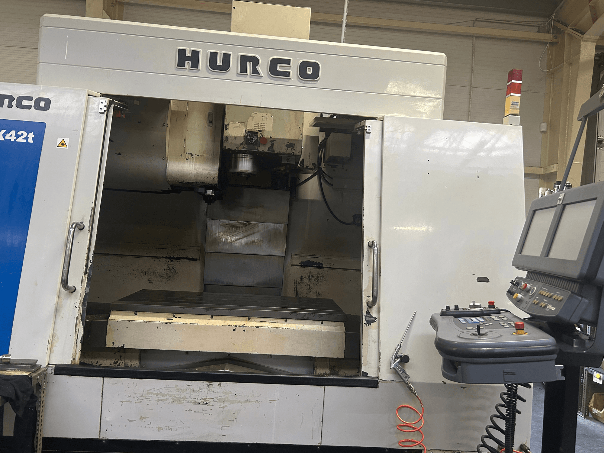 Hurco VMX42T CNC freze makinesinin önden görünümü, açık bir çalışma alanı ve düğmeli ve ekranlı kontrol paneline sahiptir.