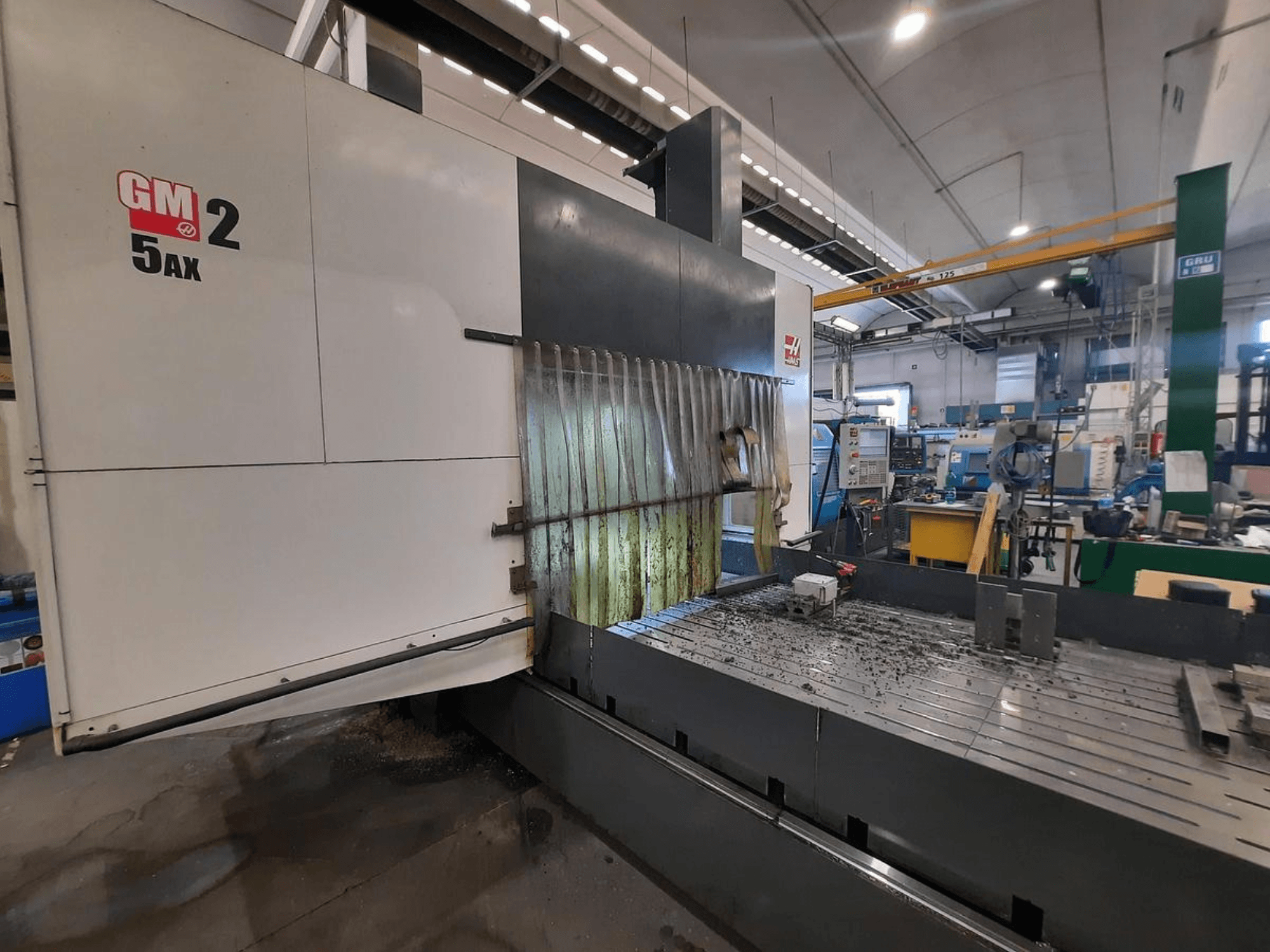 Bir atölyede GM 2 5AX CNC makinesi, yandan görünüm, çalışma alanını ve yatak yüzeyindeki metal talaşlarını gösterir.