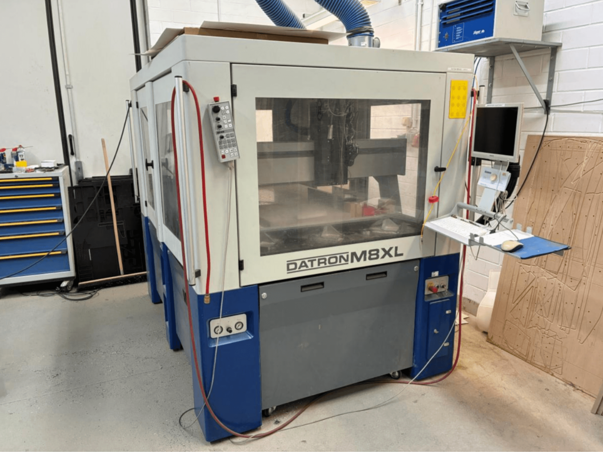 Bir atölyede DATRON M8XL CNC makinesi, kontrol paneli ve yanına monte edilmiş monitör ile önden görünüm.