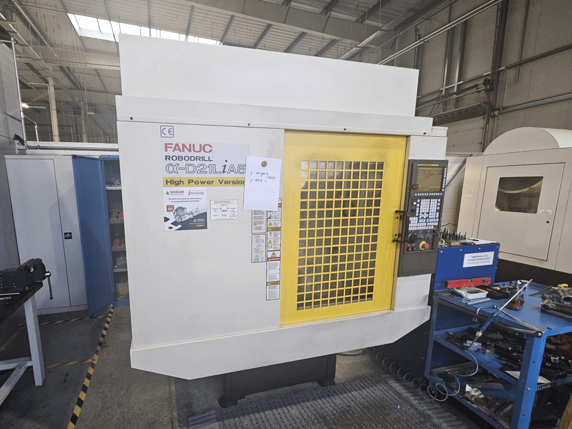 Bir FANUC Robodrill α-D21LiA5'in önden görünümü, sarı güvenlik kapısı, kontrol paneli ve çalışma alanı araçları yakındadır.