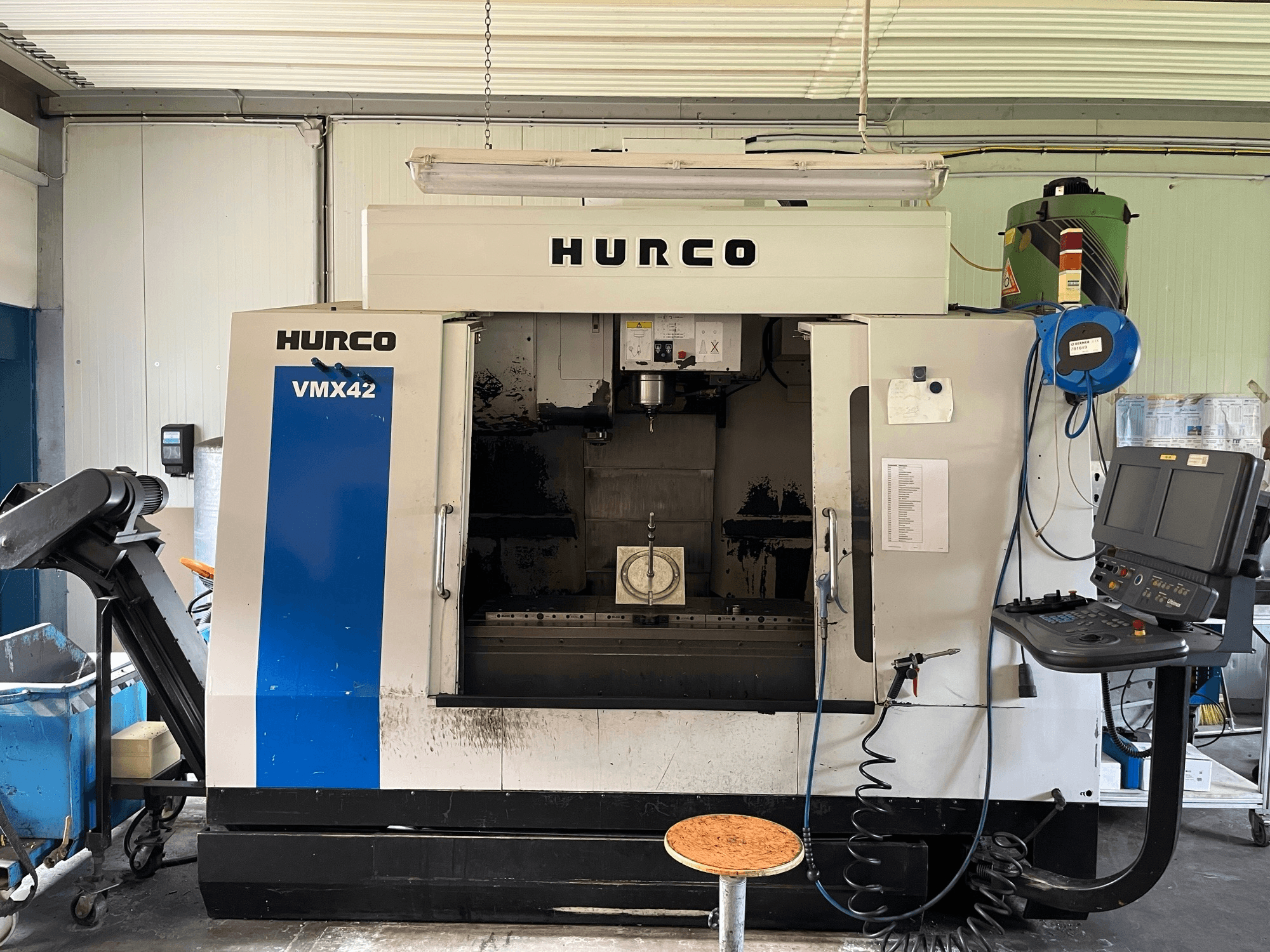 Hurco VMX 42 dikey işleme merkezinin yandan görünümü, kontrol paneli, iş mili ve iş parçası kurulumunu gösterir.
