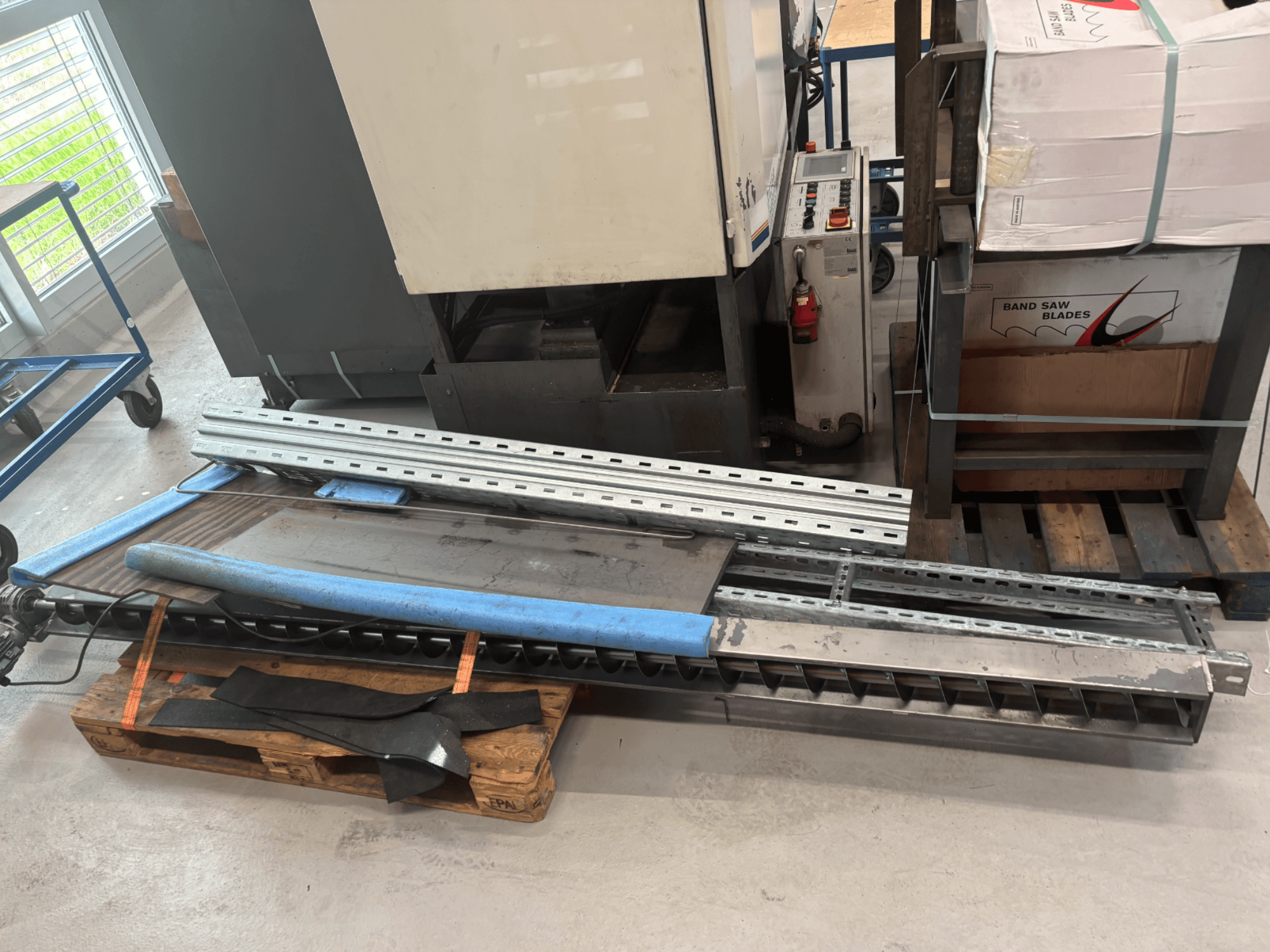 BAUER SA 430 ZA metal şerit testere, ahşap bir palet üzerinde metal çerçeve ve bileşenlerle yandan görüntülenir.