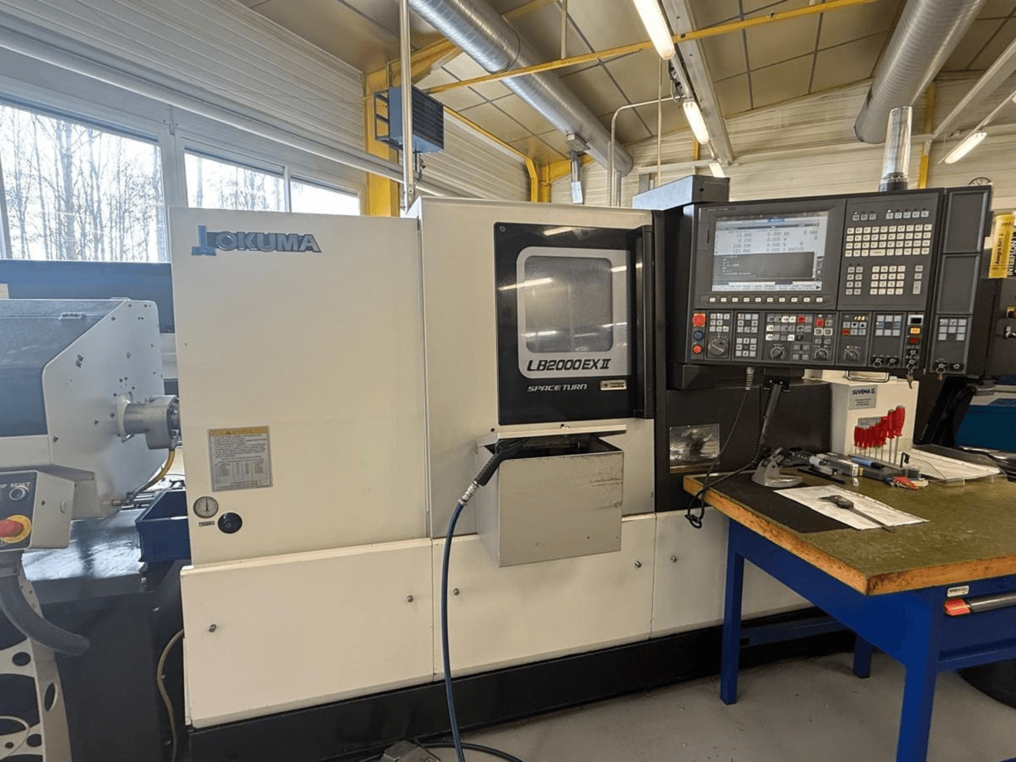 Okuma LB2000EX II yatay torna makinesi, önden görünüm; kontrol paneli, iş mili alanı ve çevresindeki çalışma alanını içerir.