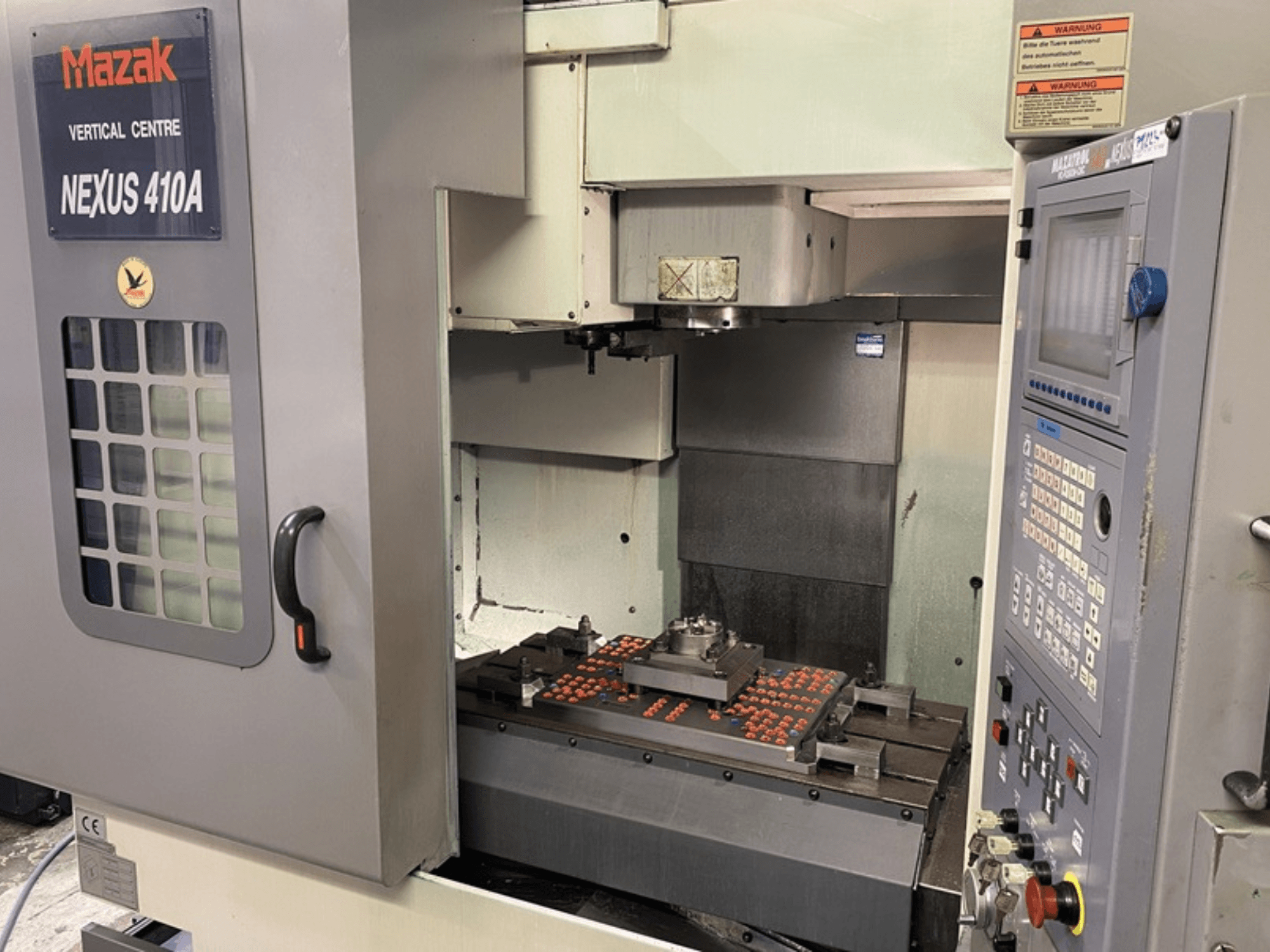 Mazak VCN410 Dik İşleme Merkezi, kontrol panelini ve iş parçası monte edilmiş makine içini gösteren önden görünüm.