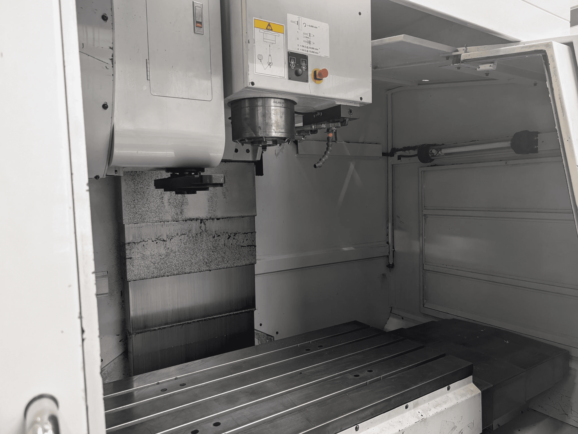 Detaylı bileşenleri ve kontrol panelini gösteren, büyük bir metal çalışma tablası ve iş mili motoruna sahip bir CNC freze makinesinin iç görünümü.