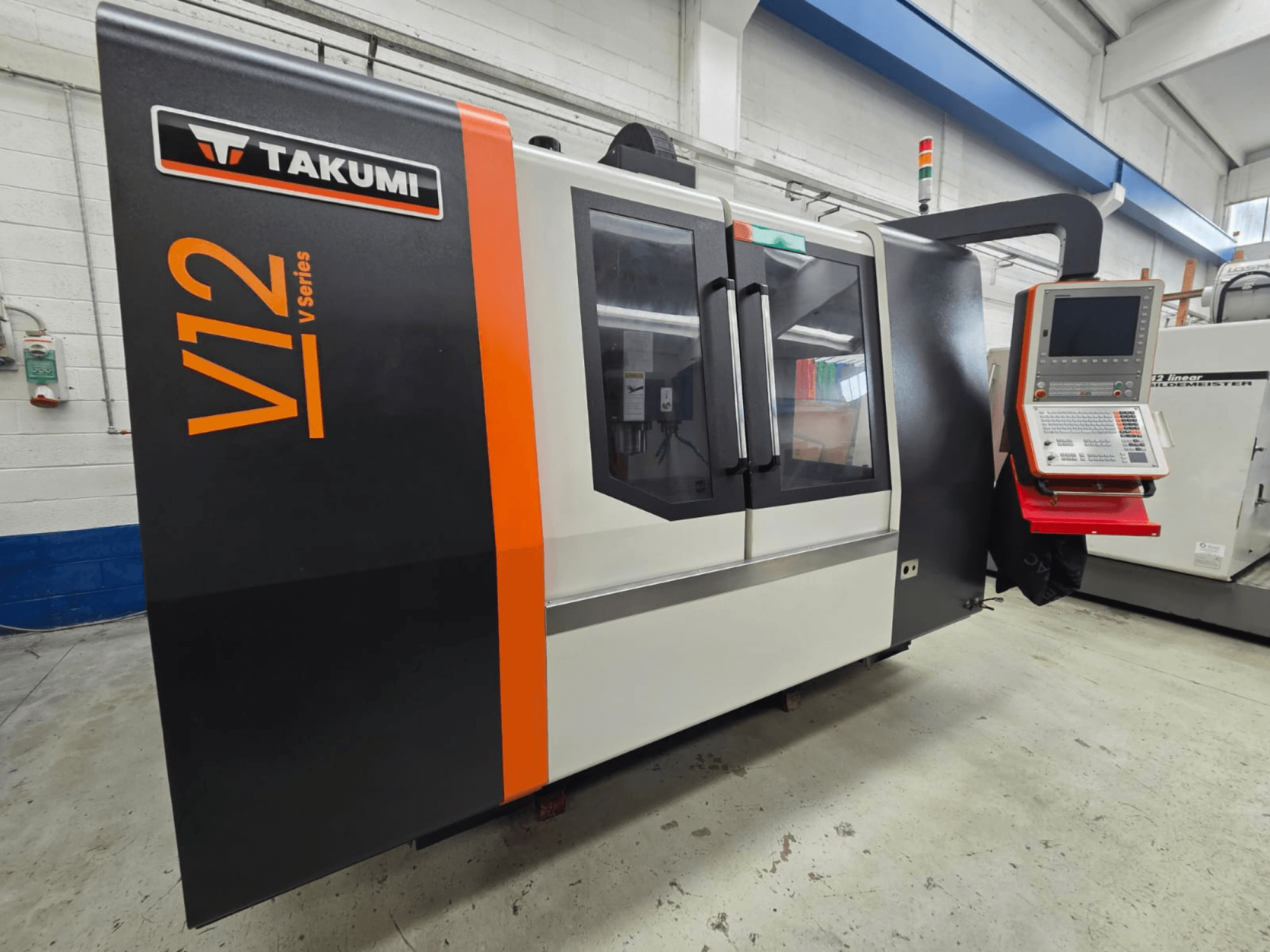 Takumi V12 V serisi CNC freze makinesi, önden görünüm, bir kontrol paneli ve büyük cam pencerelere sahiptir.