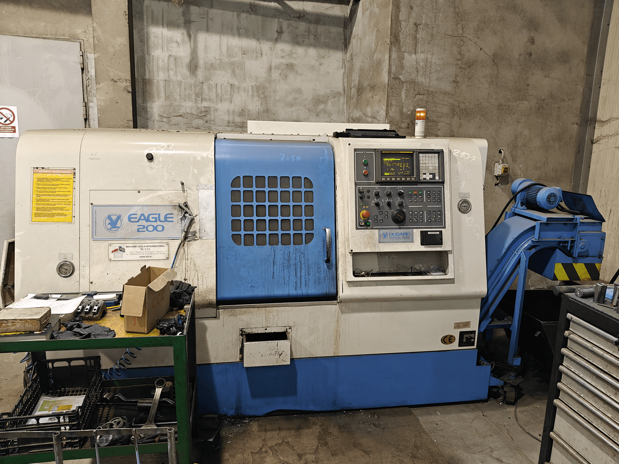 Eagle 200 CNC makinesi, kontrol paneli ile önden görünüm, yeşil bir araba üzerinde çeşitli aletler. Görünür aşınma ve çalışma ışıkları.