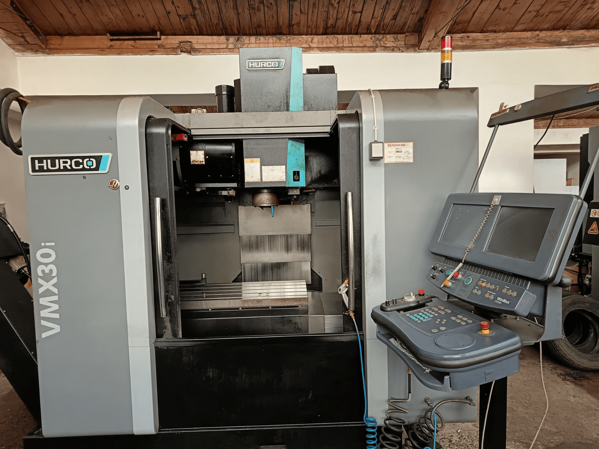 HURCO VMX30i işleme merkezinin önden görünümü, düğmeli ve monitörlü kontrol paneli, metalik çalışma alanı ve uyarı ışığı.