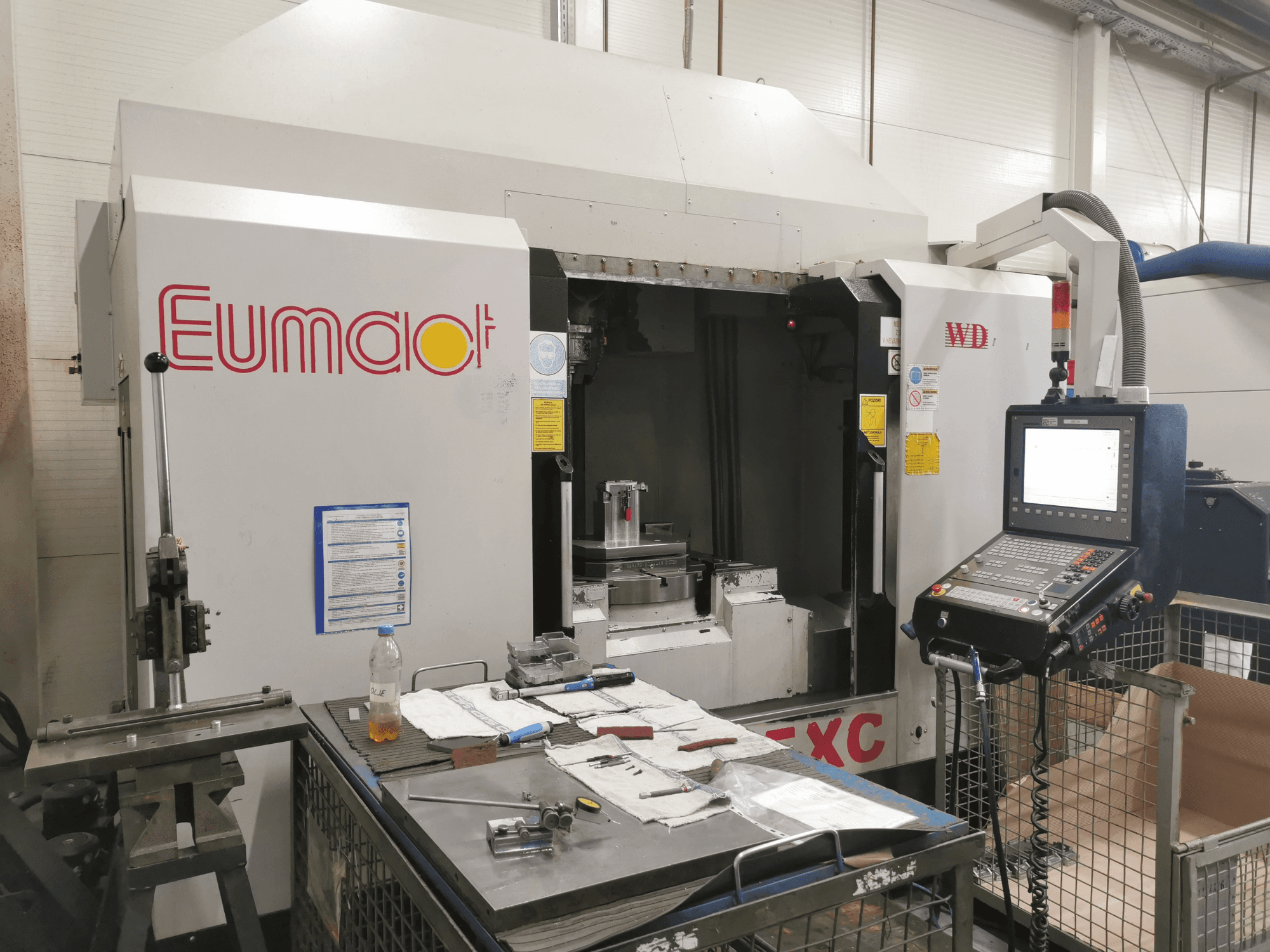 Kontrol paneli, aletler ve bileşenler ve malzemelerle dolu bir çalışma yüzeyi ile bir Eumdaot CNC makinesinin önden görünümü.
