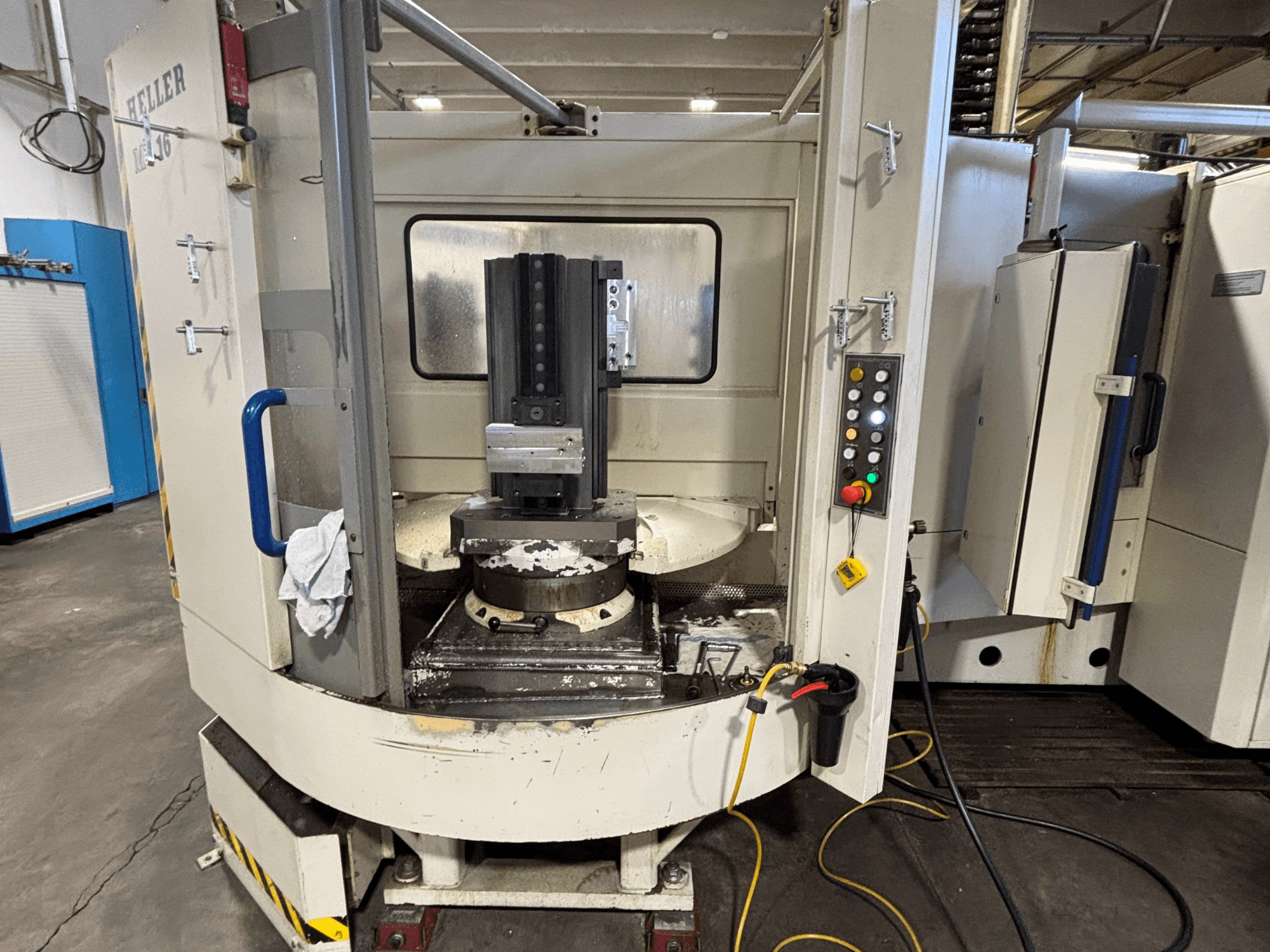 Heller işleme merkezi, model dikey, iş milini, kontrol panelini ve ekipman takılı çalışma masasını gösteren önden görünüm.