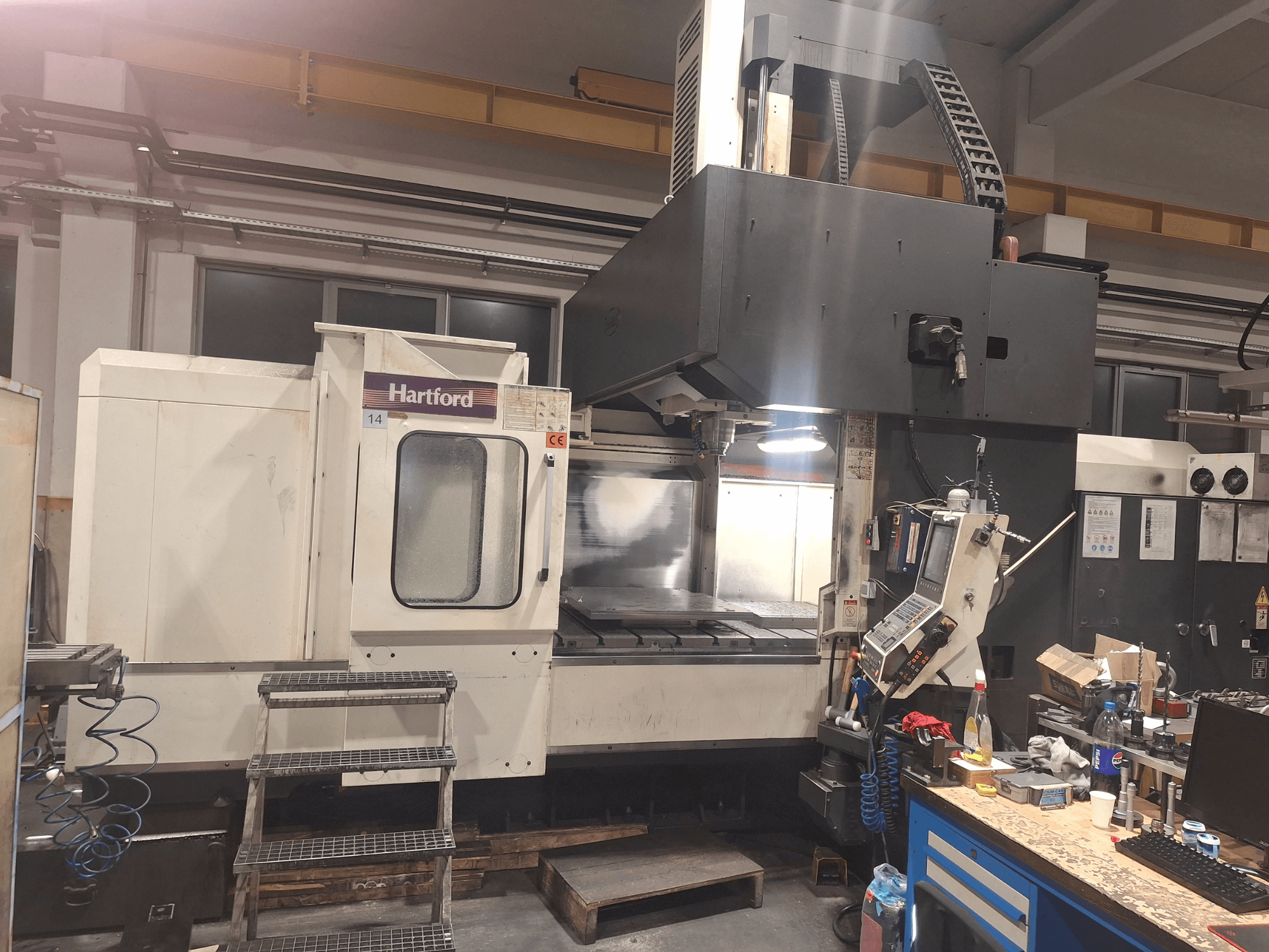 Hartford CNC makinesi, önden görünüm, teknik kontroller, erişim için basamaklar ve bir atölye ortamında çalışma masası alanı.