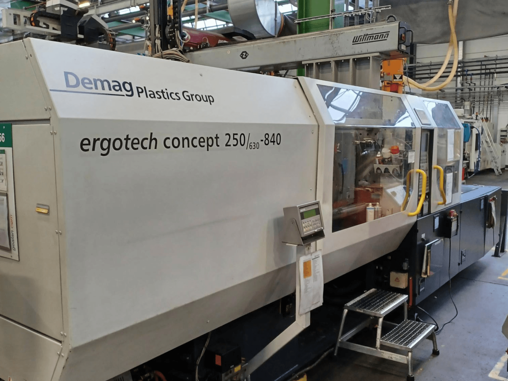 Demag ergotech concept 250/630-840 enjeksiyon kalıplama makinesi, önden görünüm, dijital kontrolleri ve şeffaf güvenlik kapaklarını gösterir.