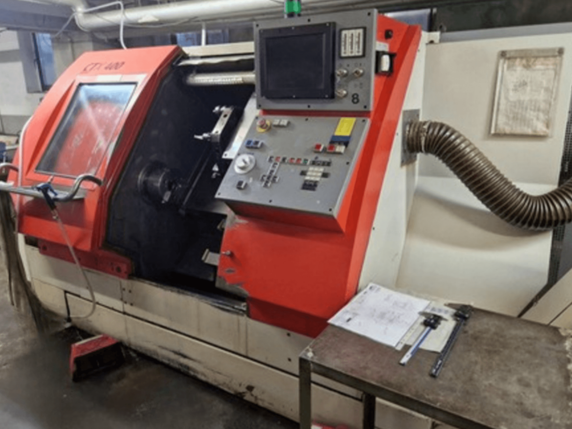Gildemeister CTX 400 yatay torna makinesinin önden görünümü, kontrol paneli, açık kapı ve aletli atölye masası.