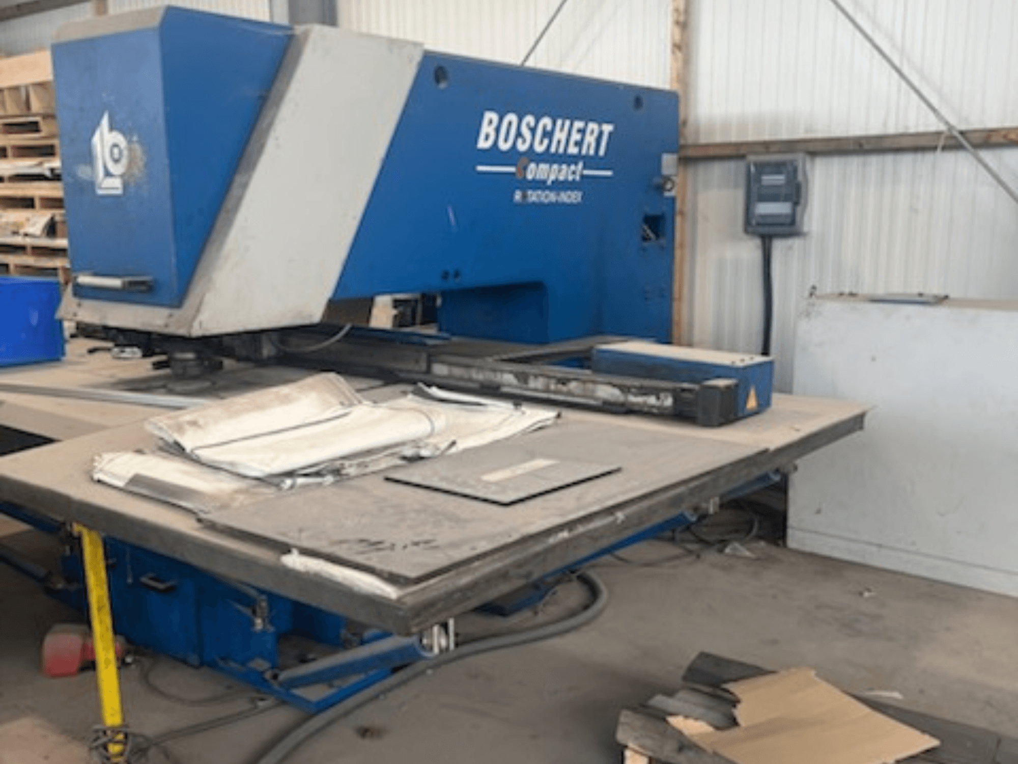 Bir atölyede bulunan BOSCHERT COMPACT 1000 CNC delme makinesi; masanın üzerinde metal levhaların bulunduğu önden görünüm.