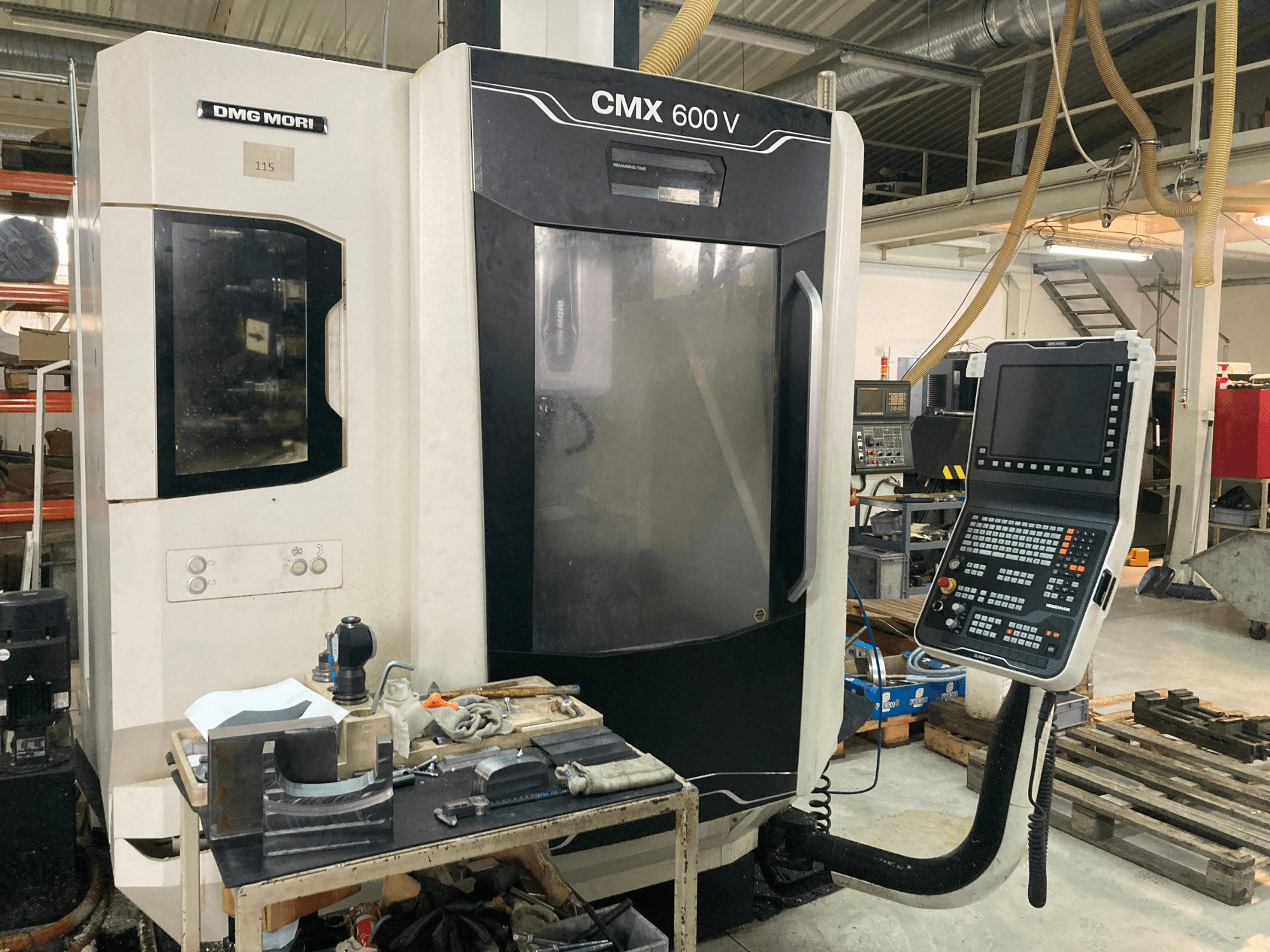 DMG MORI CMX 600 V freze makinesinin önden görünümü, kontrol panelini ve takımların bulunduğu çalışma masasını gösterir.