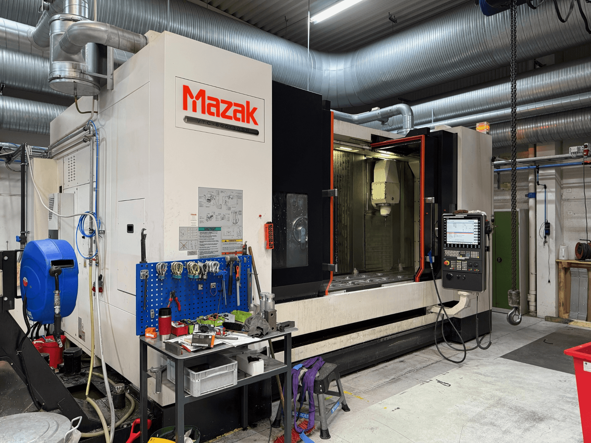Önden görünümlü Mazak CNC makinesi, bir işleme ortamında kontrolleri, araçları ve çalışma alanını içerir.