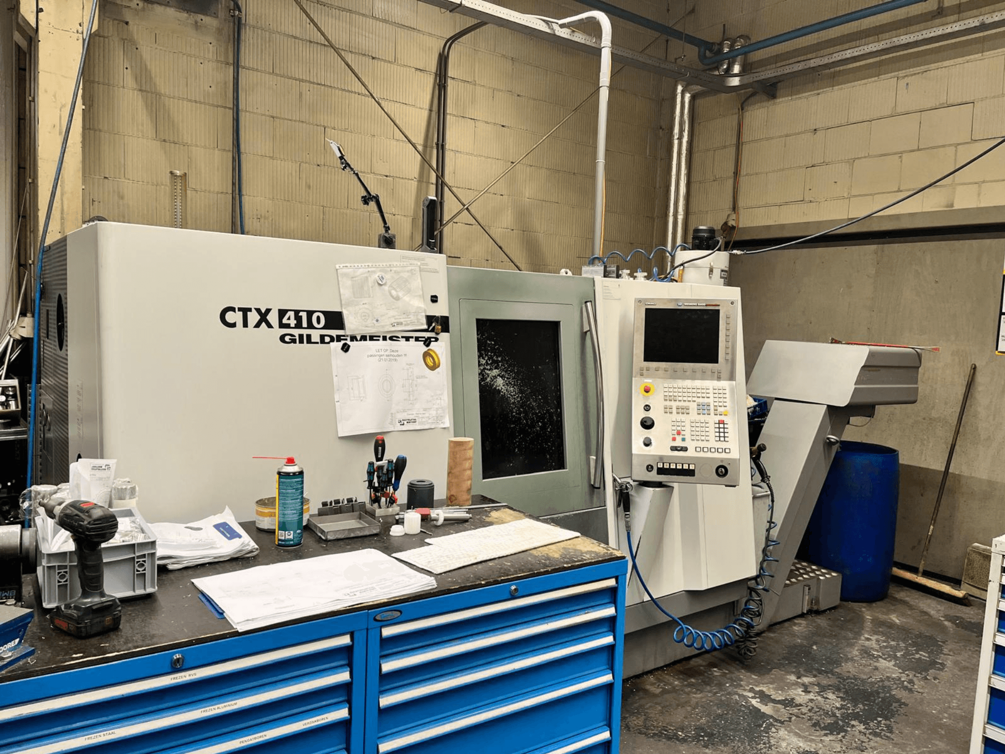 Bir atölyede Gildemeister CTX 410 CNC makinesi, önden görünüm, bir kontrol paneli ve bir tezgah üzerinde çeşitli aletler.