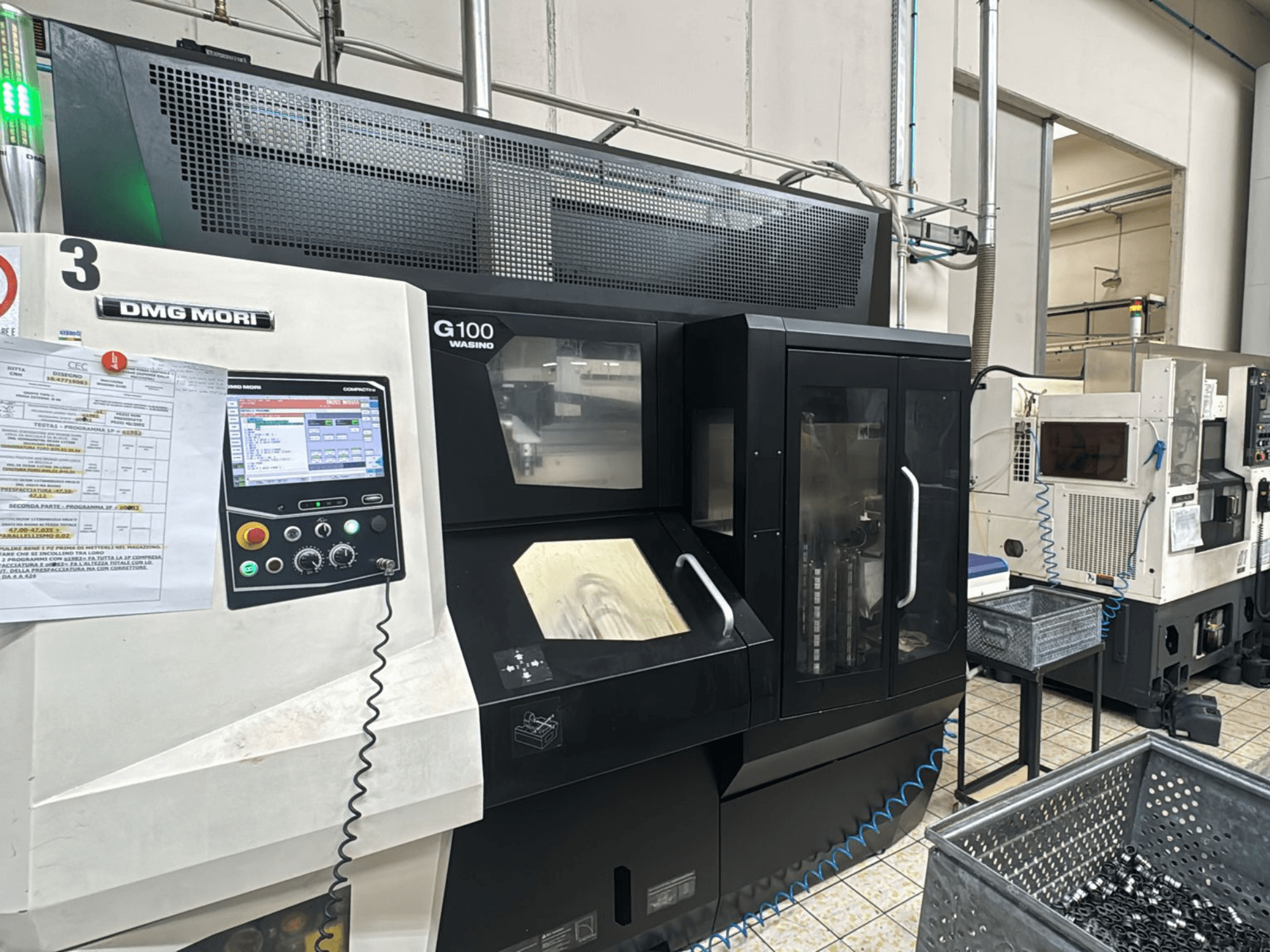 Fabrikadaki DMG MORI G100 makinesi, önden görünüm, dijital kontrol paneli ve yakındaki takım saklama kutuları.