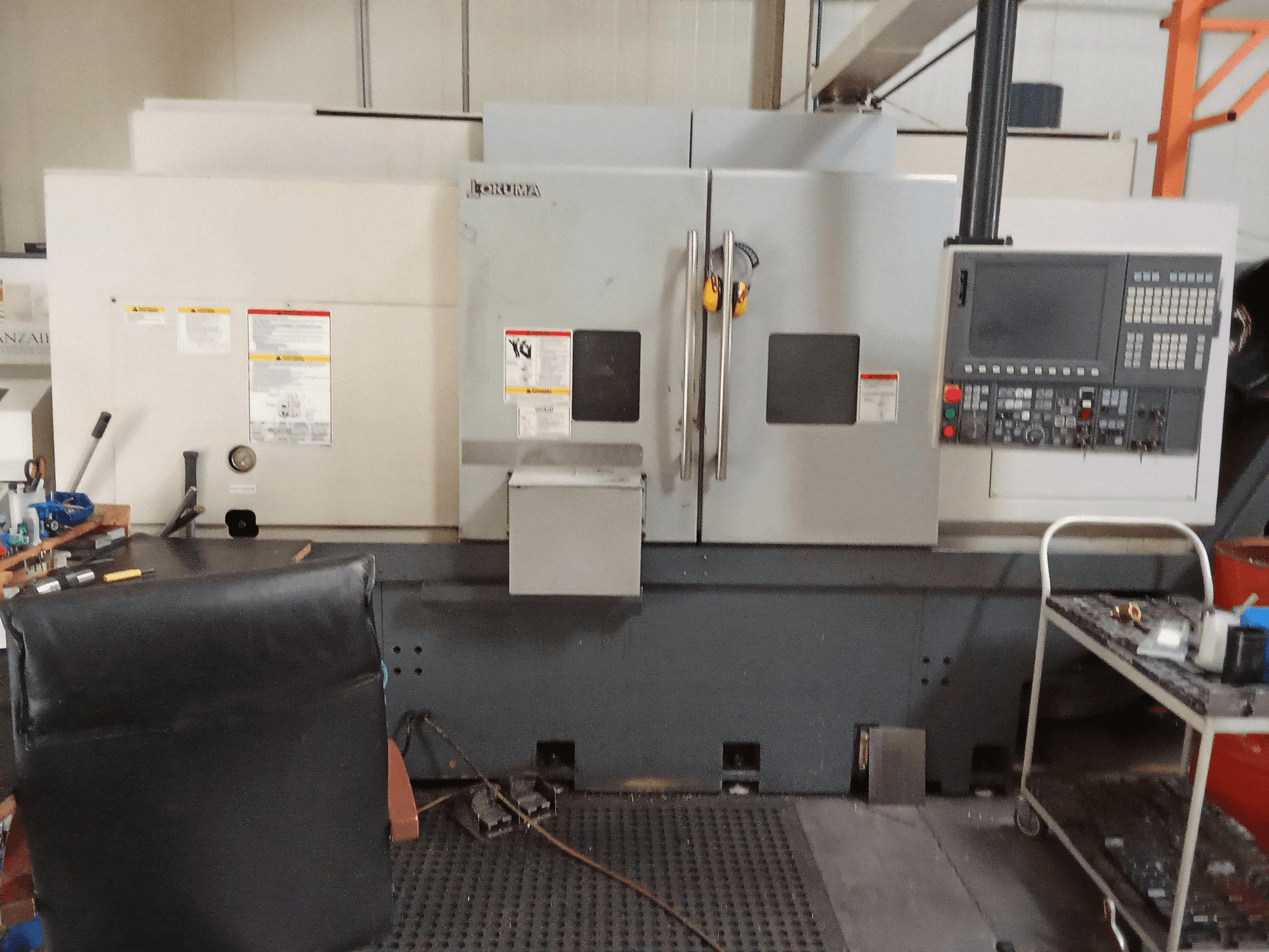 Okuma Genos L300 E-M yatay torna makinesinin önden görünümü, kontrol paneli ve çift kapısı atölye ortamında sergilenmektedir.