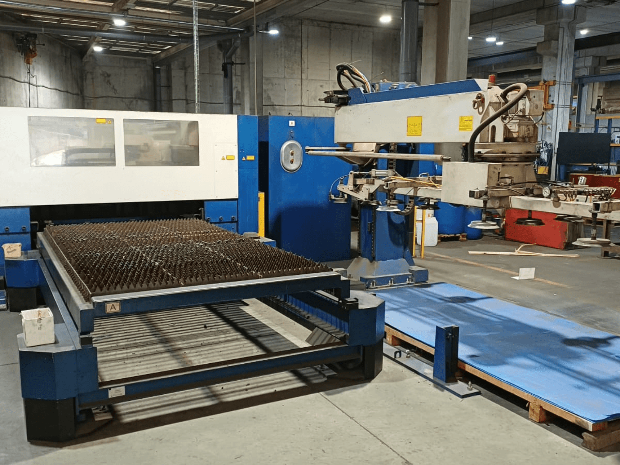 TRUMPF TRUMATIC L 3030 CO₂ lazer kesim makinesi, yandan görünüm; çivili yüzeyli kesim masası ve robot kolu gösterilmektedir.