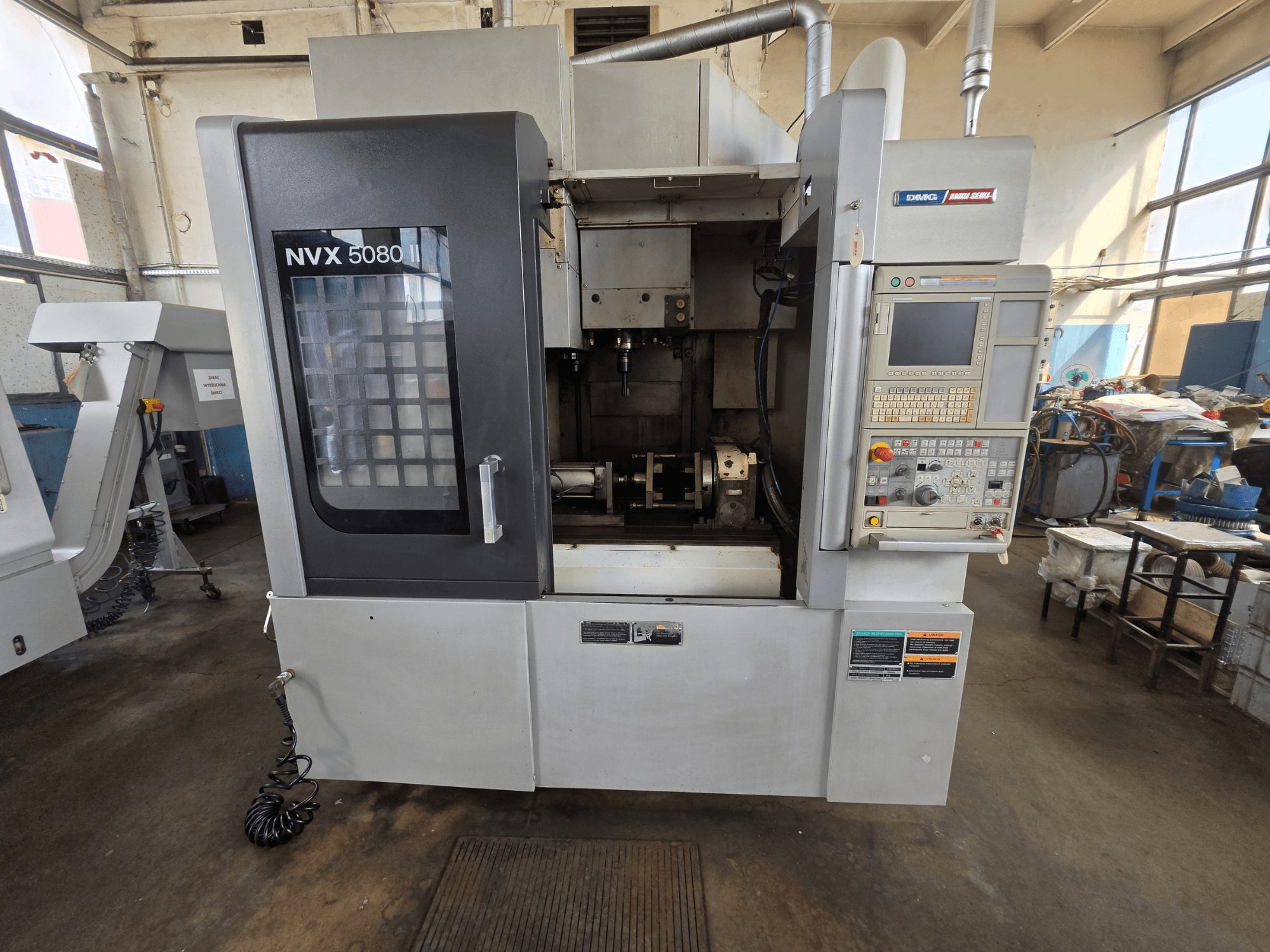 DMG Mori Seiki NVX 5080 II/40 dikey işleme merkezinin, kontrol paneli ve işleme alanını gösteren şeffaf pencereye sahip önden görünümü.