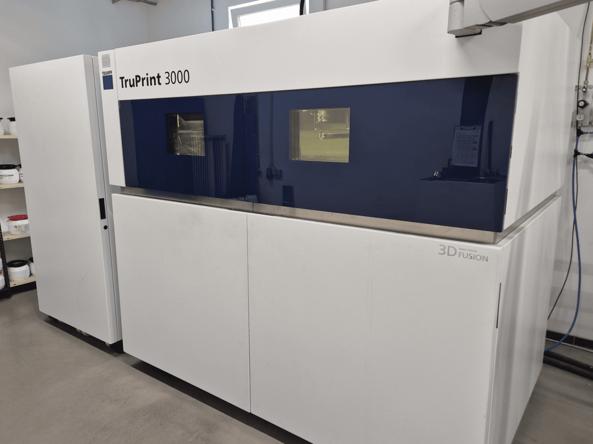 Mavi panelli tasarıma ve lazer füzyon teknolojisine sahip TruPrint 3000 metal 3D yazıcının önden görünümü.