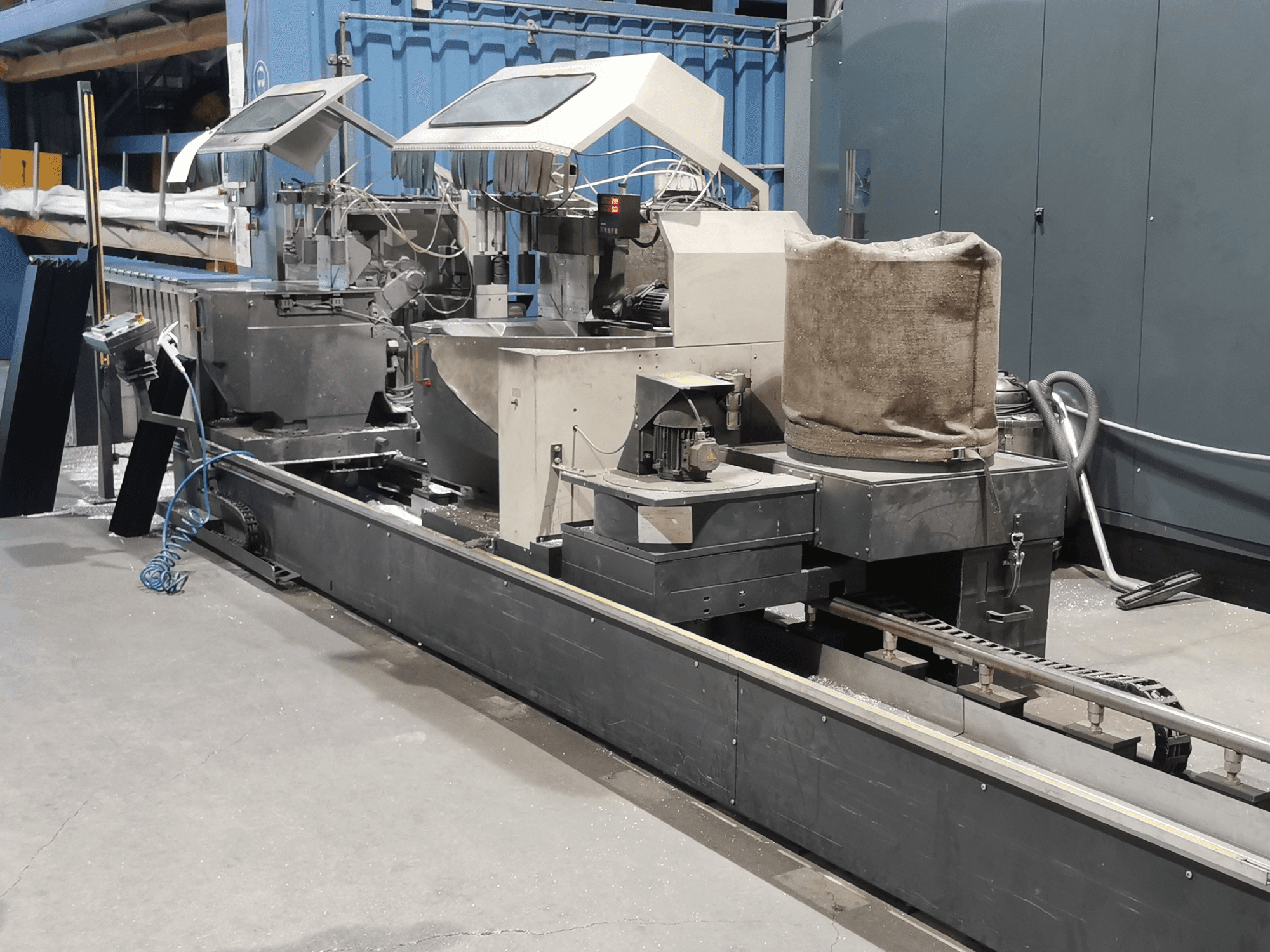 Fabrika ortamında hazneleri, konveyör bandı ve kontrol paneli ile yandan görüntülenen endüstriyel işleme makinesi.