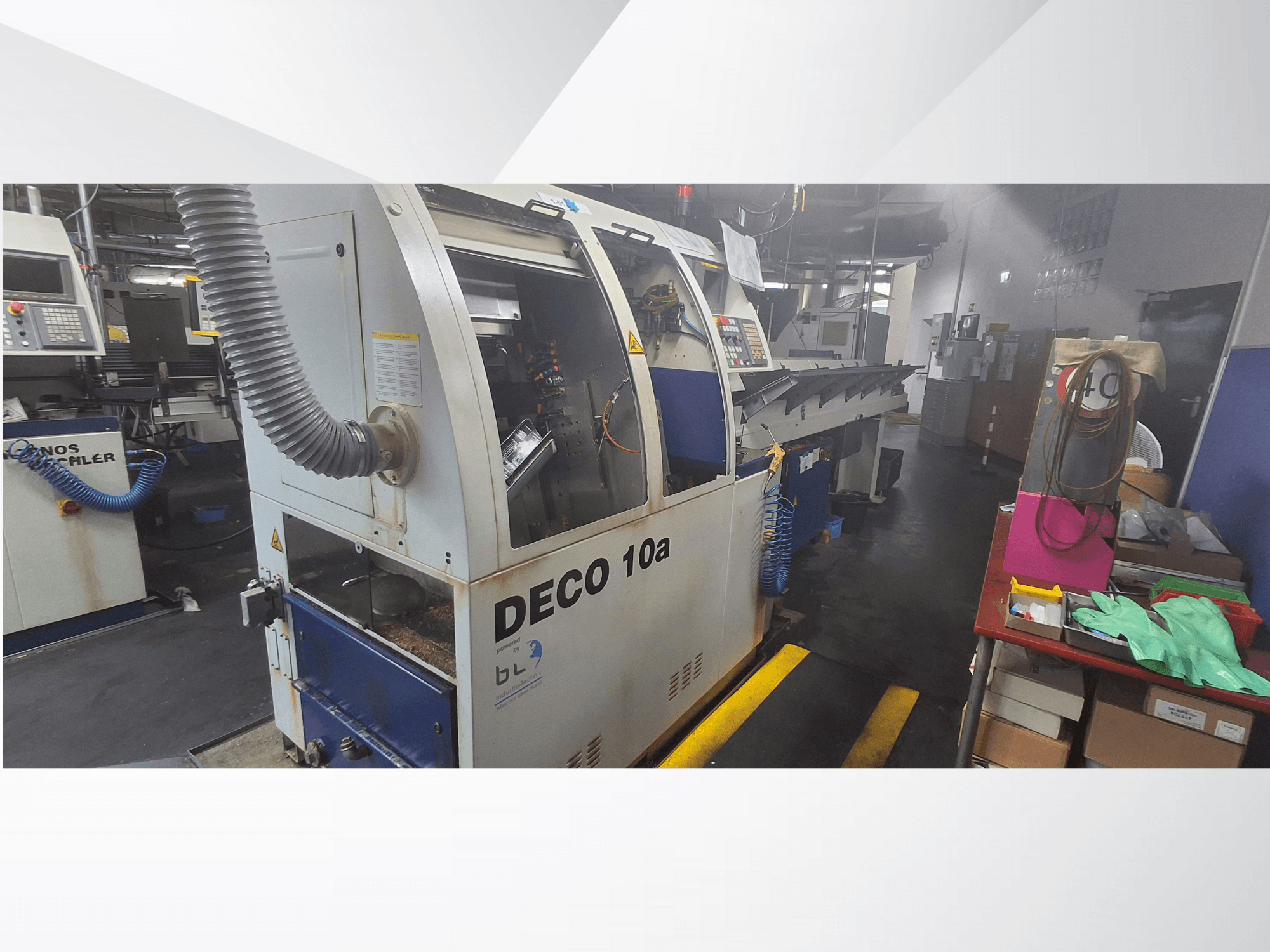 DECO 10a CNC makinesi atölyede, önden görünüm; kontrol paneli ve toz emme sistemine sahiptir, yanında çalışma tezgahı vardır.