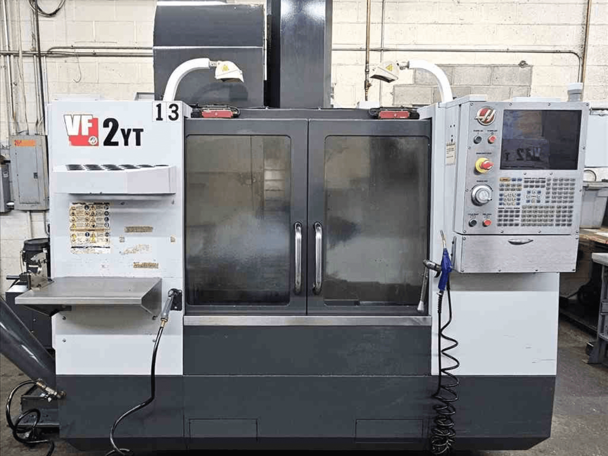 HAAS VF-2YT Dik İşleme Merkezinin önden görünümü, kontrol paneli ve cam kapılar.