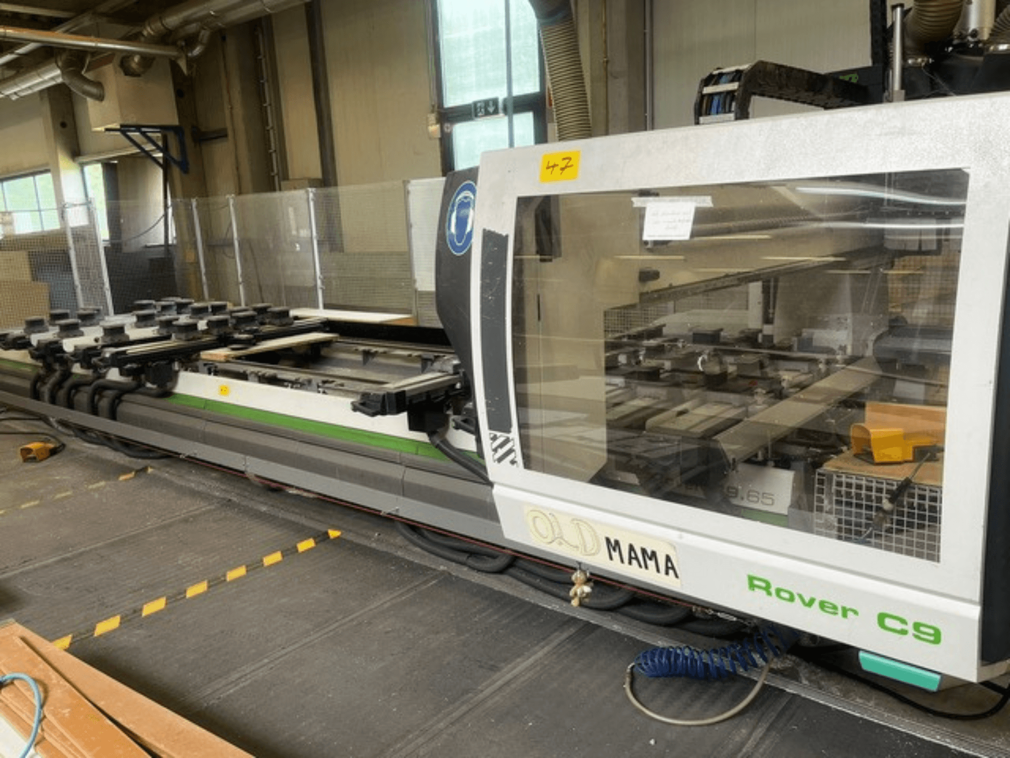 BIESSE Rover C 9.65 CNC router bir atölyede, kontrol panelini ve kelepçeli çalışma masasını gösteren yandan görünüm.