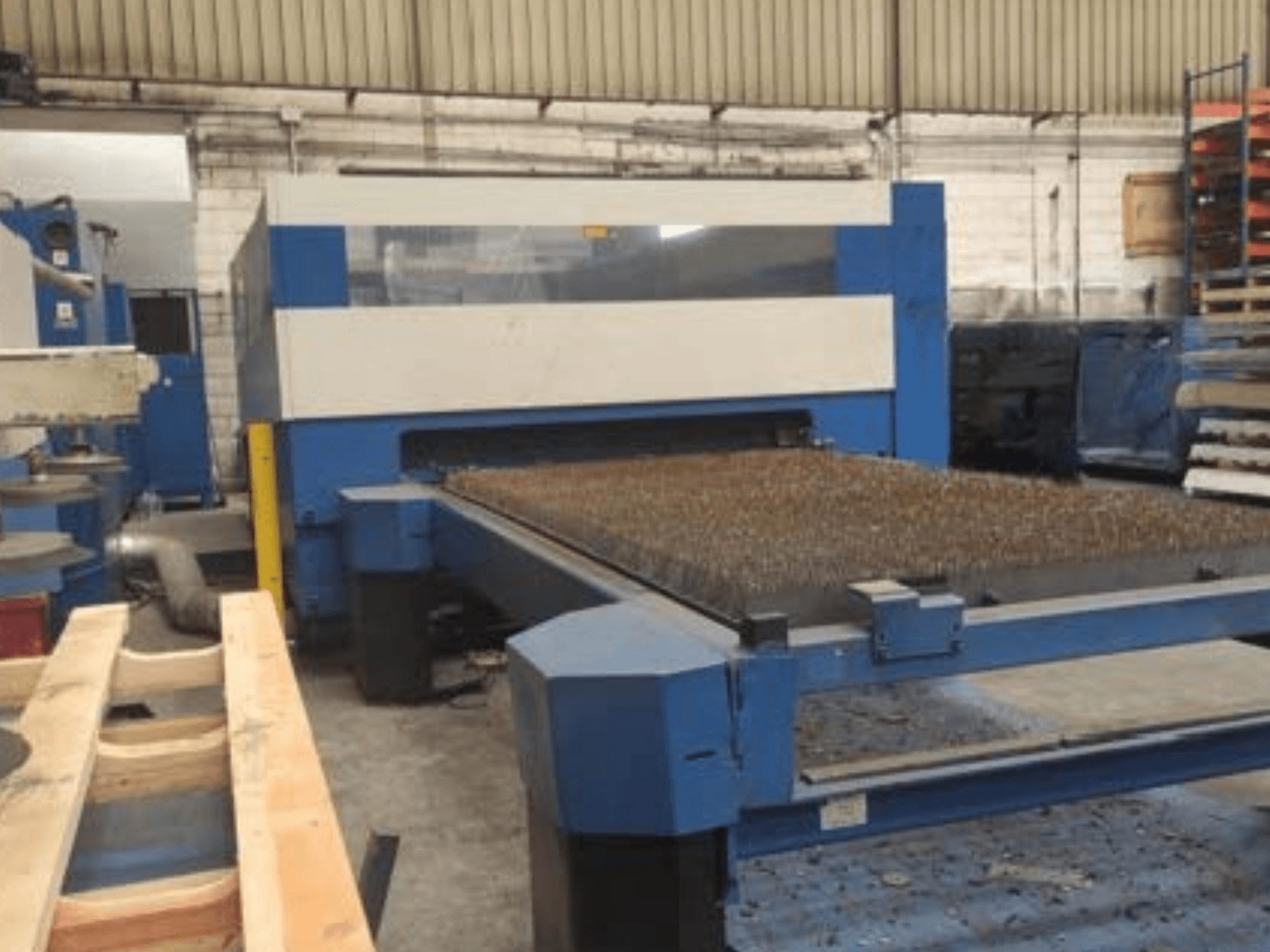 Dokulu metal yataklı mavi lazer kesim makinesi, yandan görünüm, endüstriyel bir çalışma alanındaki operasyonel kurulumu gösteriyor.