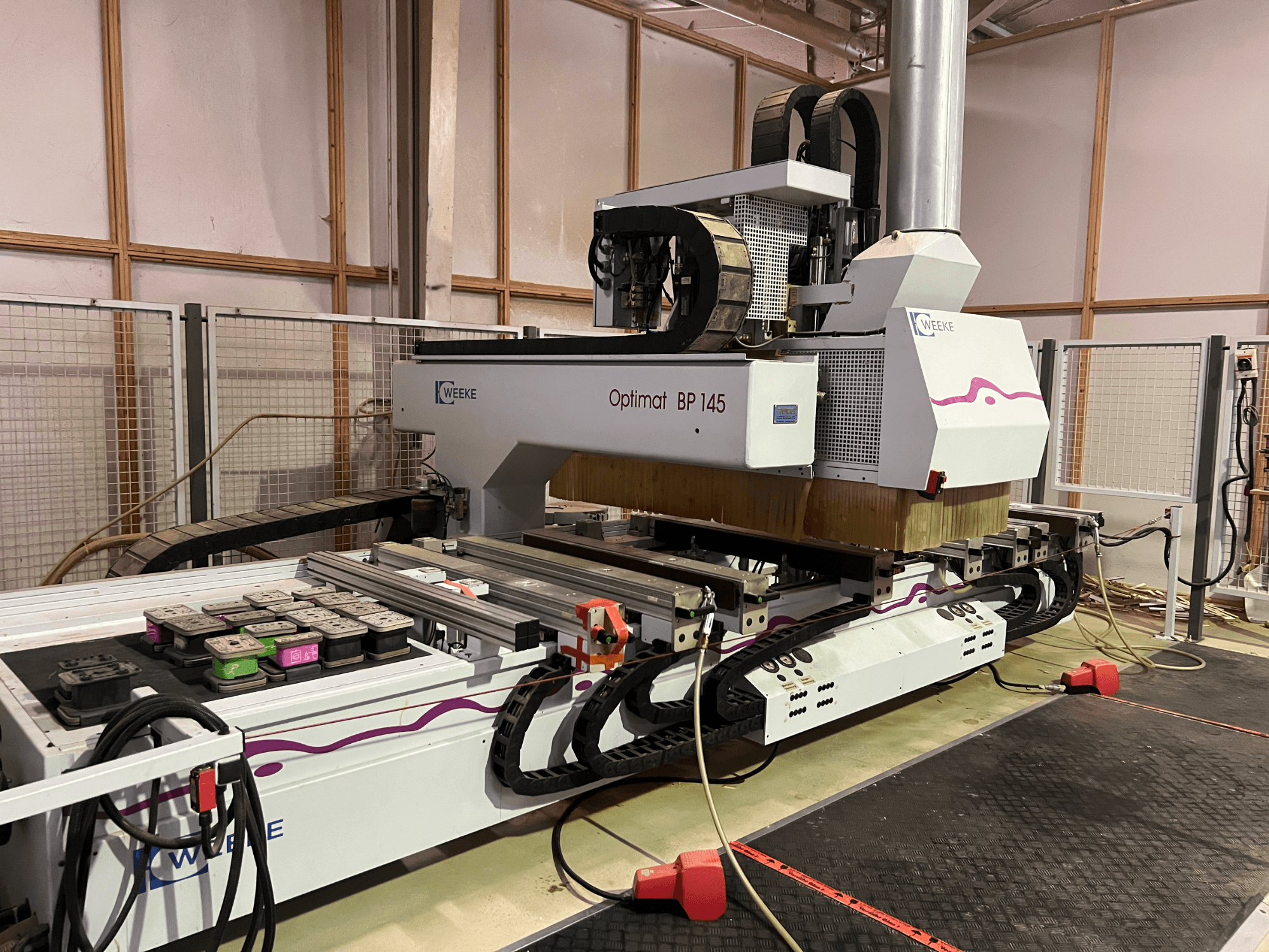 WEEKE Optimat BP 145 bir fabrikada, yandan bakıldığında kontrol düğmeleri ve kabloları olan bir CNC makinesini sergiliyor.