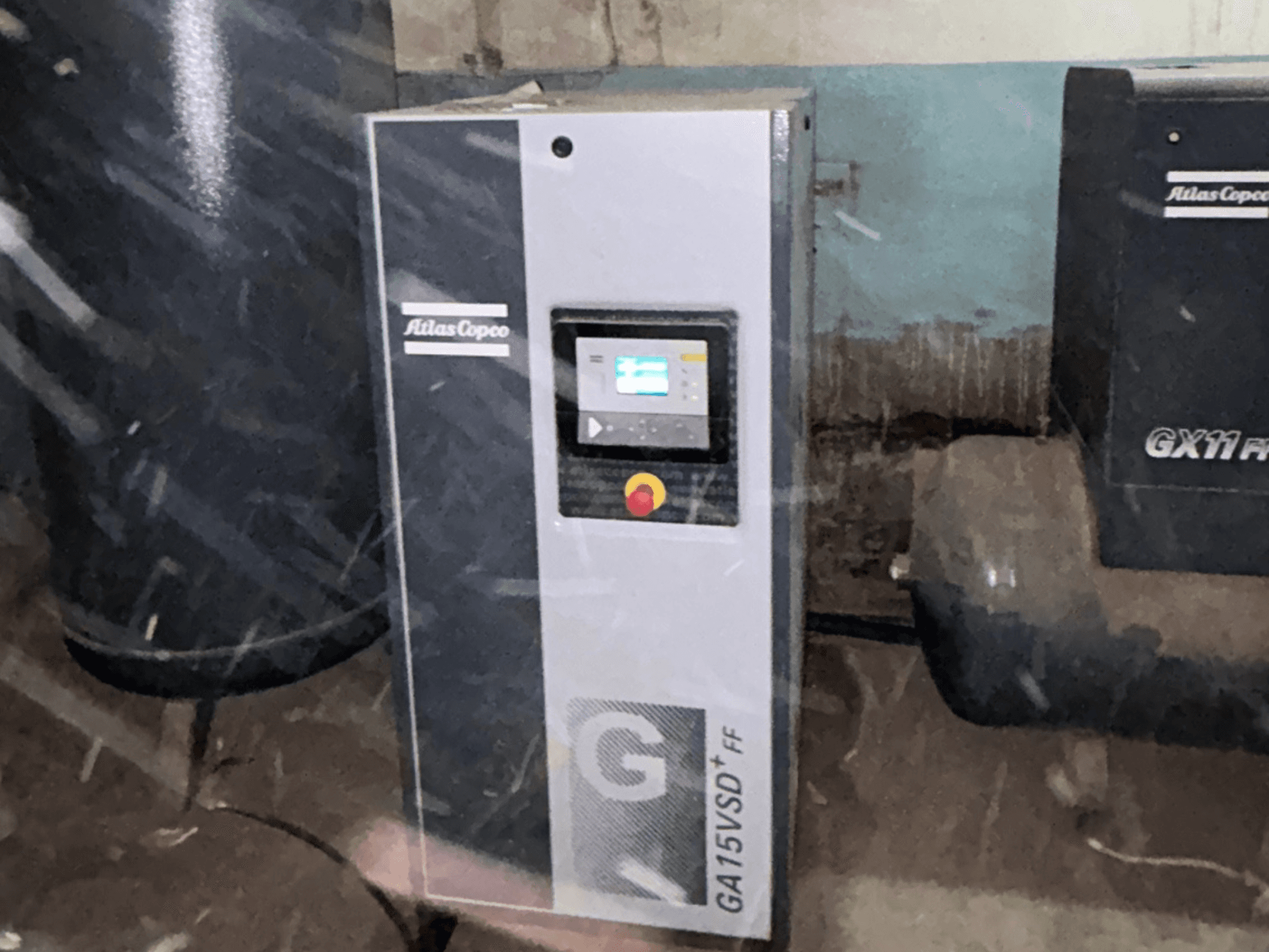 Atlas Copco GA15VSD+FF hava kompresörü, önden görünüm; ekranlı kontrol paneli ve kırmızı acil durdurma düğmesi içerir.