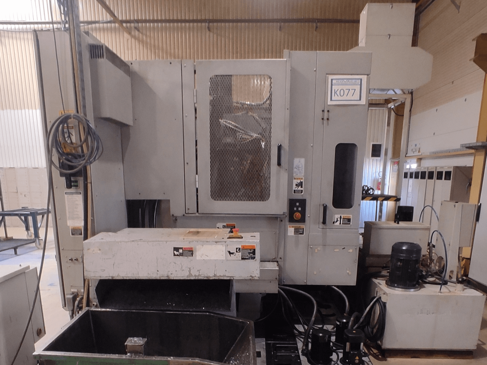 Büyük bir çalışma tezgahına sahip gri endüstriyel CNC makinesi, yandan görünüm, kontrol paneli ve soğutucu haznesi, model K077.