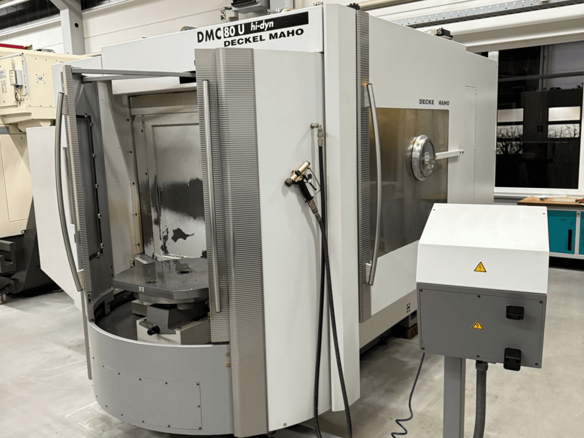 Yan tarafında açık erişim kapısı ve kontrol paneli bulunan Deckel Maho DMC 80 U yüksek hızlı CNC freze makinesinin önden görünümü.