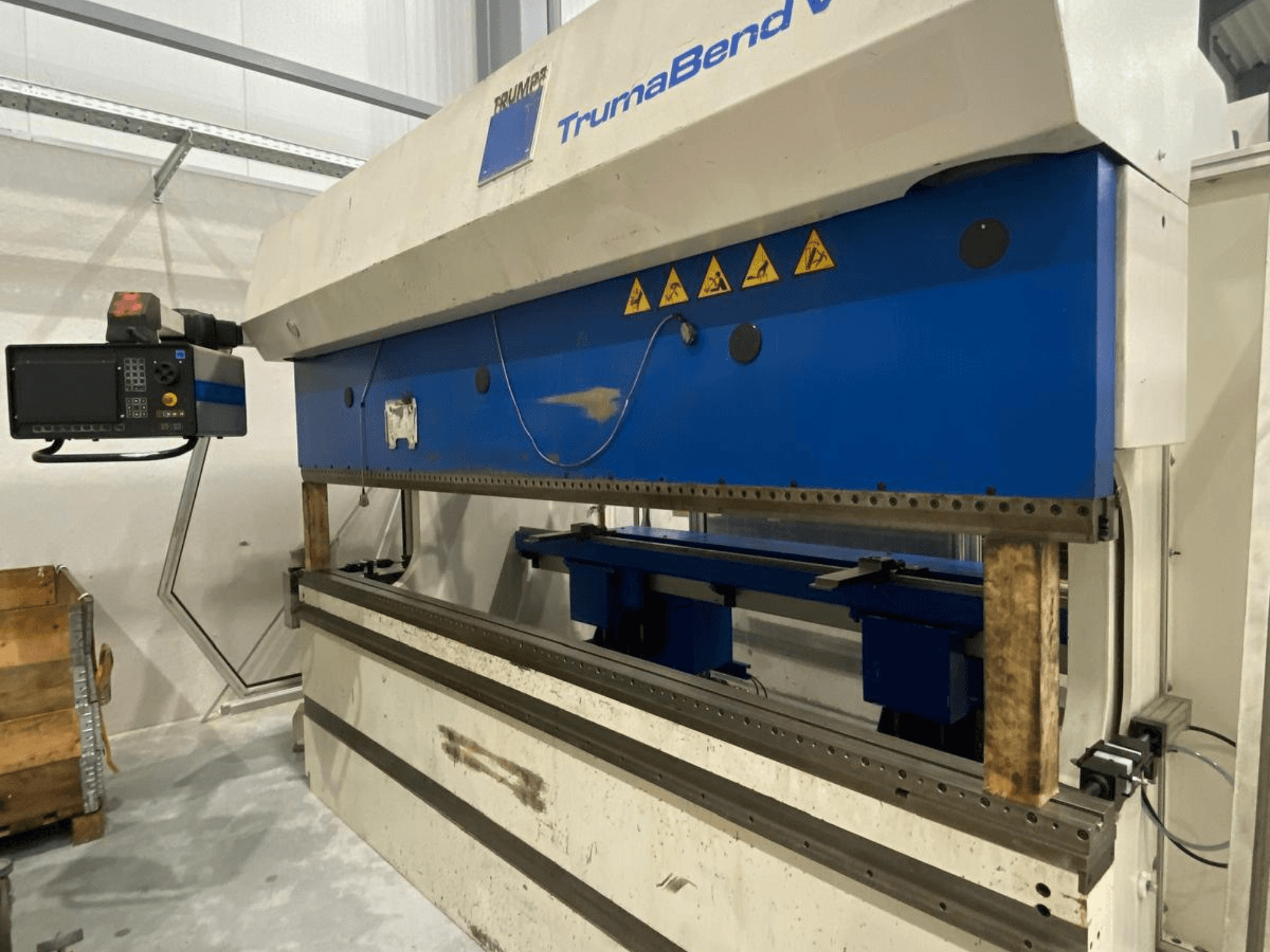TRUMPF Trumabend V130 kant press, önden görünüm; kontrol paneli, mavi parçalar ve güvenlik uyarı etiketleri görülebilir.
