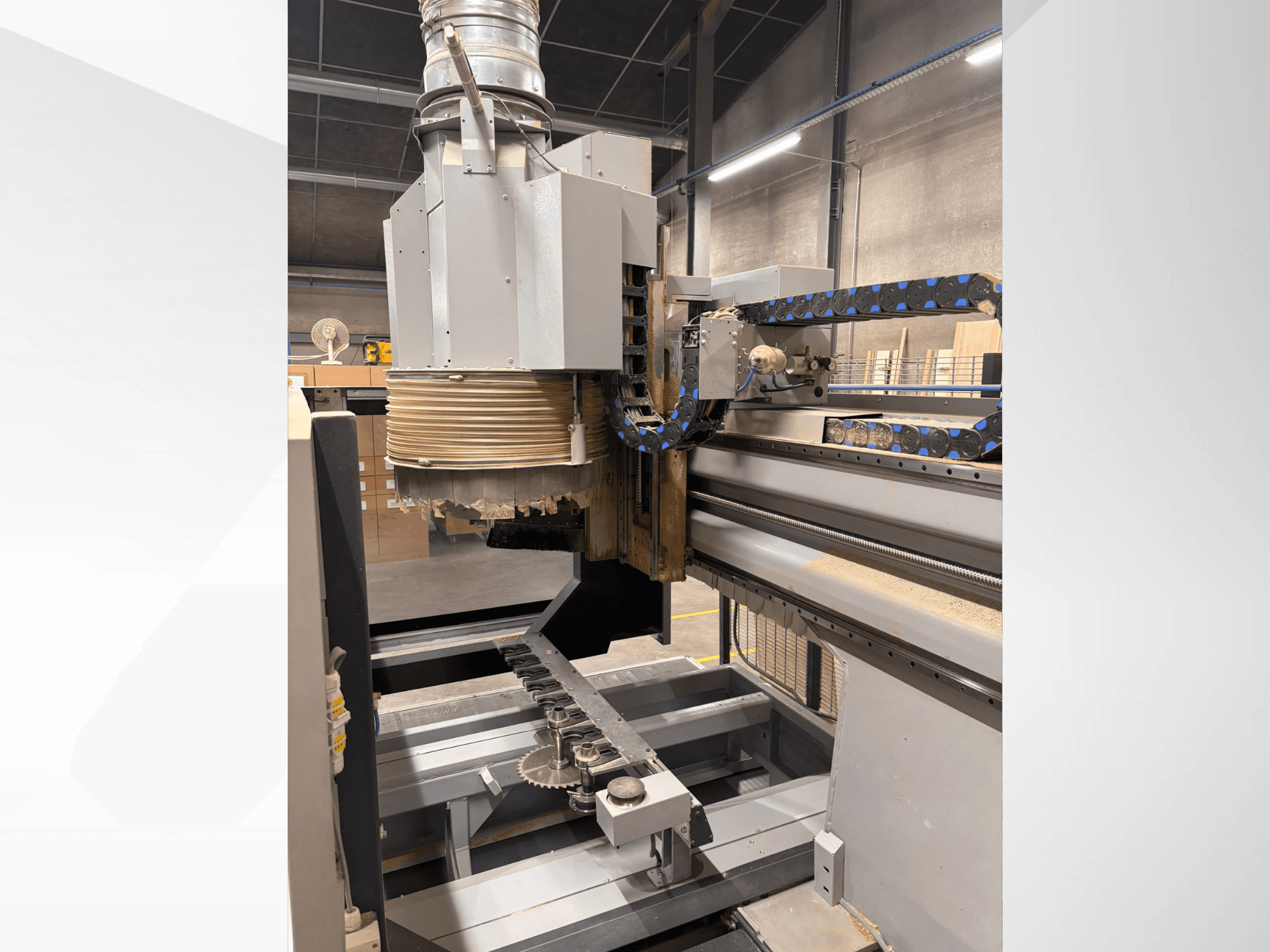 Büyük bir iş mili ve konveyöre sahip CNC router makinesi, yandan görünüm, ahşap kesme aletlerini ve makine bileşenlerini gösterir.