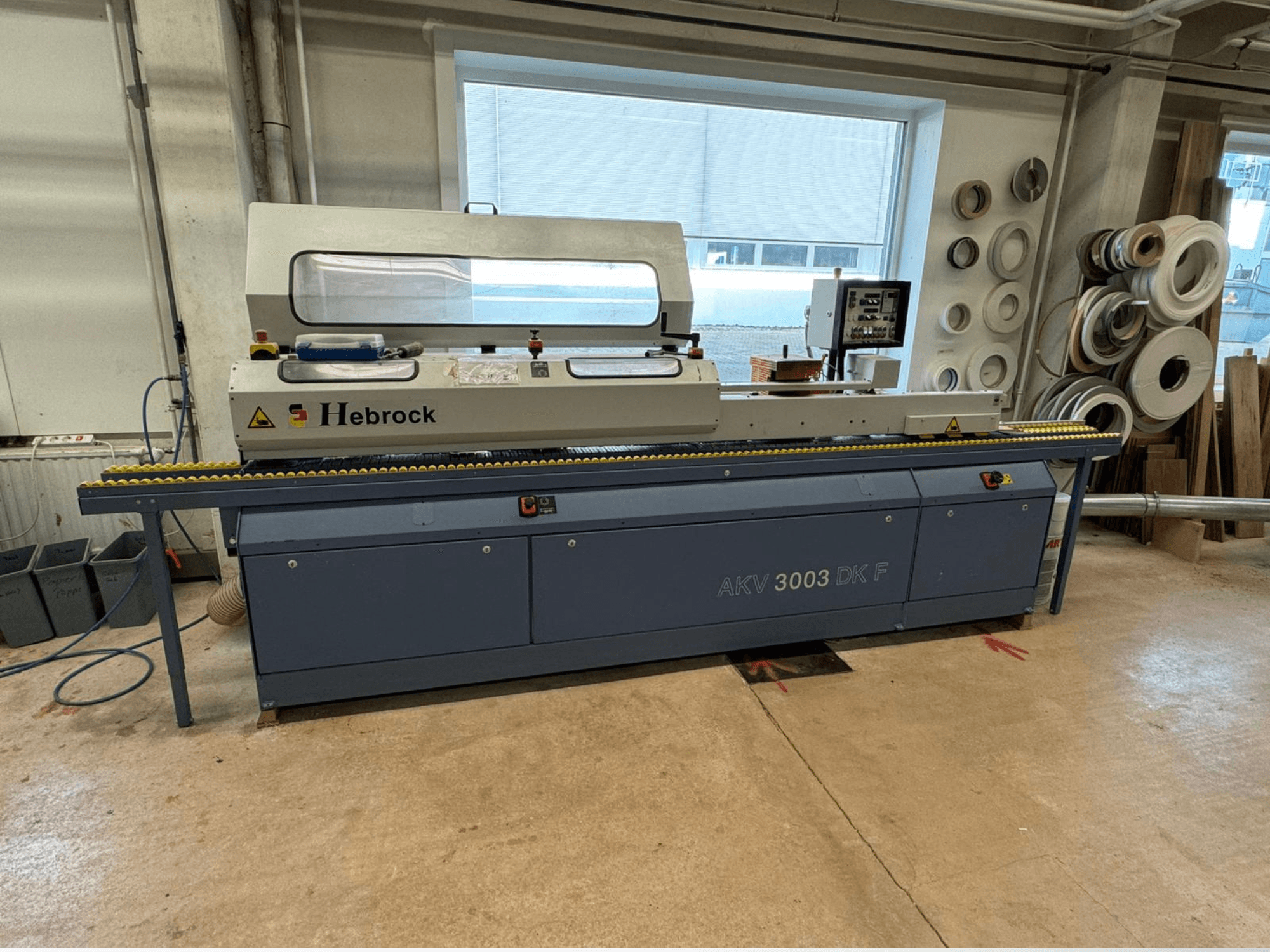 Hebrock AKV 3003 DK F kenar bantlama makinesi, önden görünüm, bir atölyede bulunan bir konveyör ve kontrol paneline sahiptir.