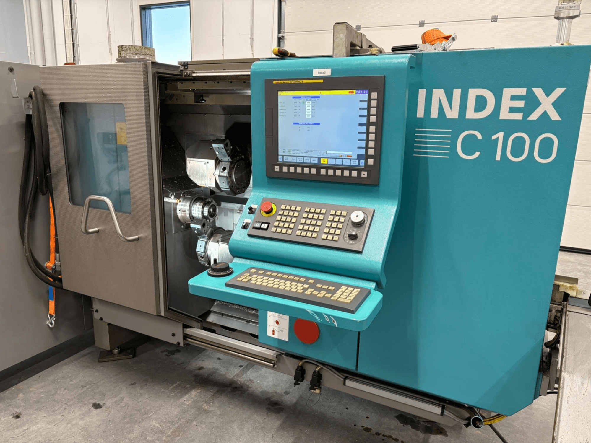 Index C100 İsviçre Tipi Torna Tezgahının kontrol paneli ve iç bileşenleri gösteren açık muhafazası ile önden görünümü.