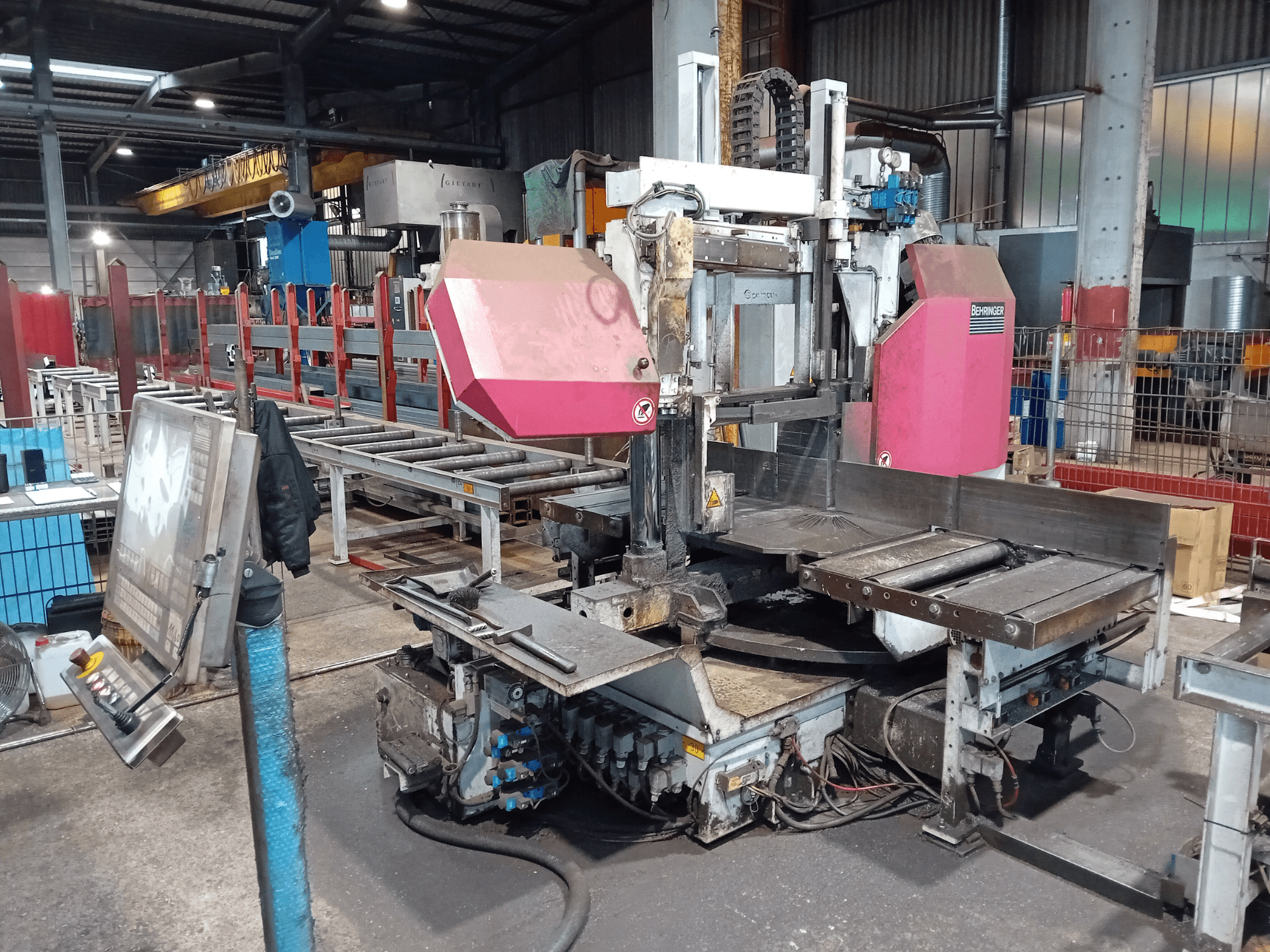 Bir fabrikadaki Behringer şerit testere makinesi, önden görünüm, büyük bir kesme bıçağı ve düğmeli kontrol paneli.