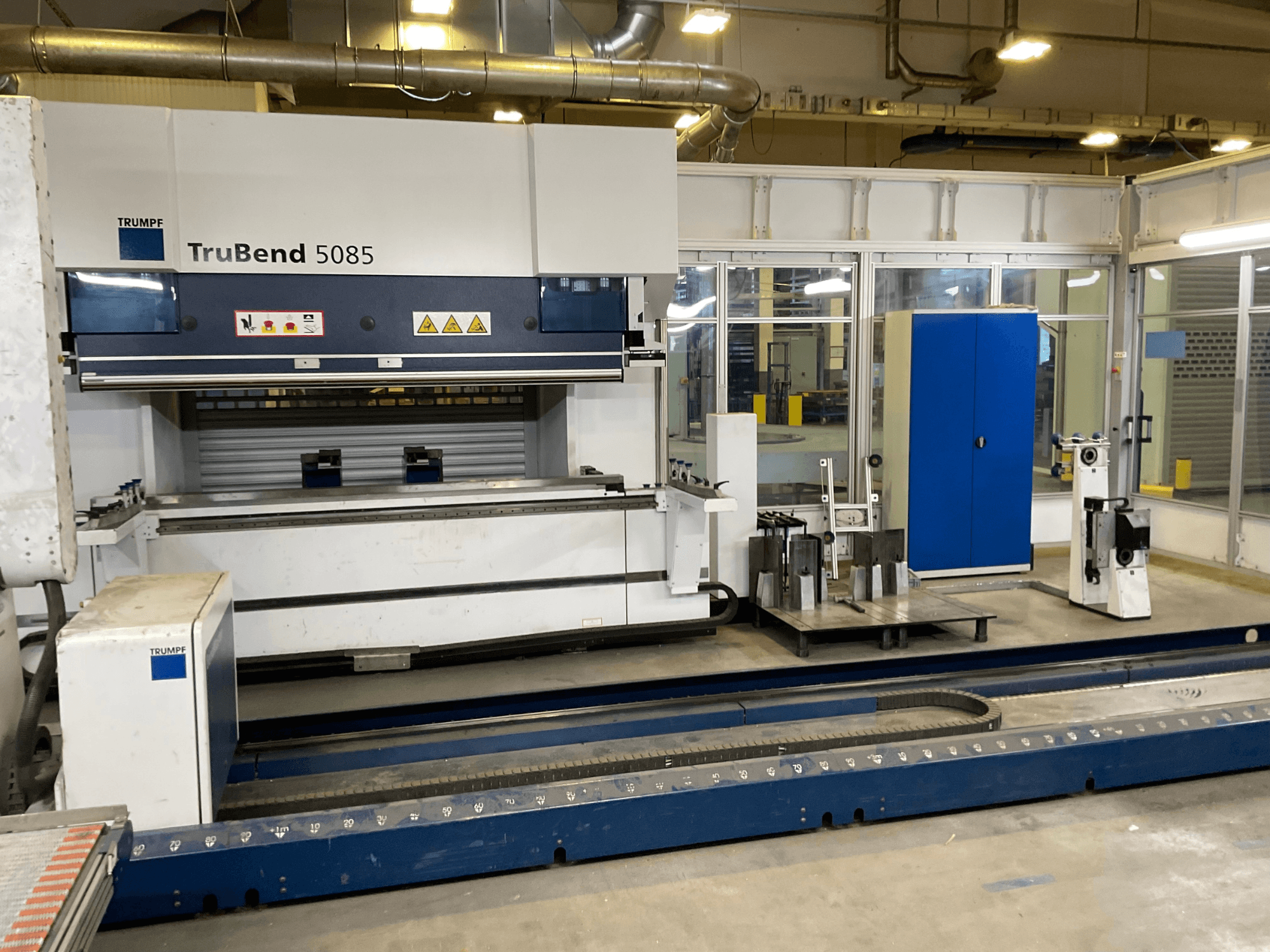 TRUMPF TruBend 5085, kontrol paneli ve yanında çeşitli aletler bulunan büyük bir metal bükme makinesinin yandan görünümü.
