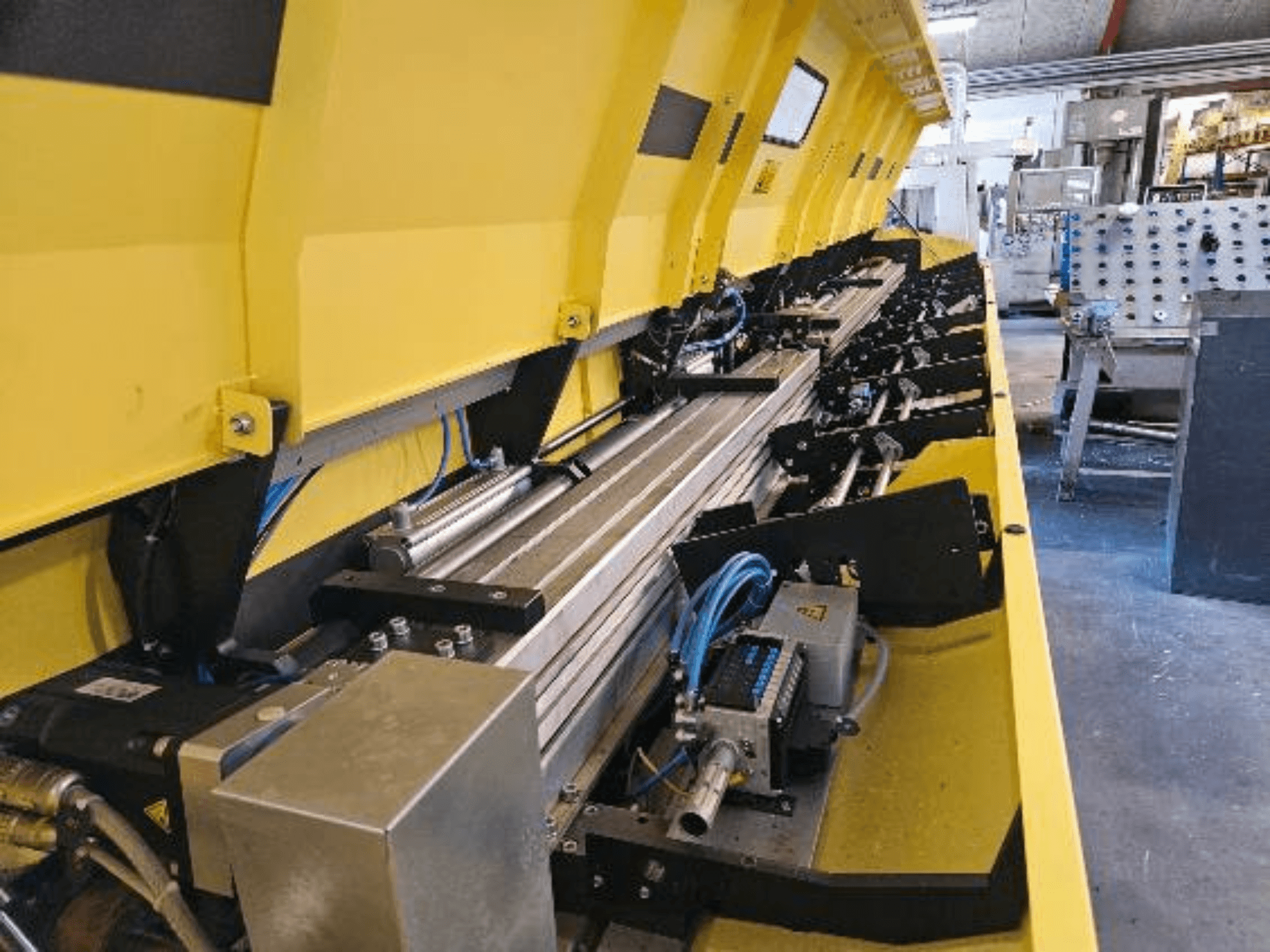 Hortumlar ve elektronik parçalar içeren, metalik bileşenlere ve konveyör raylarına sahip sarı bir hidrolik makinenin yakından görünümü.