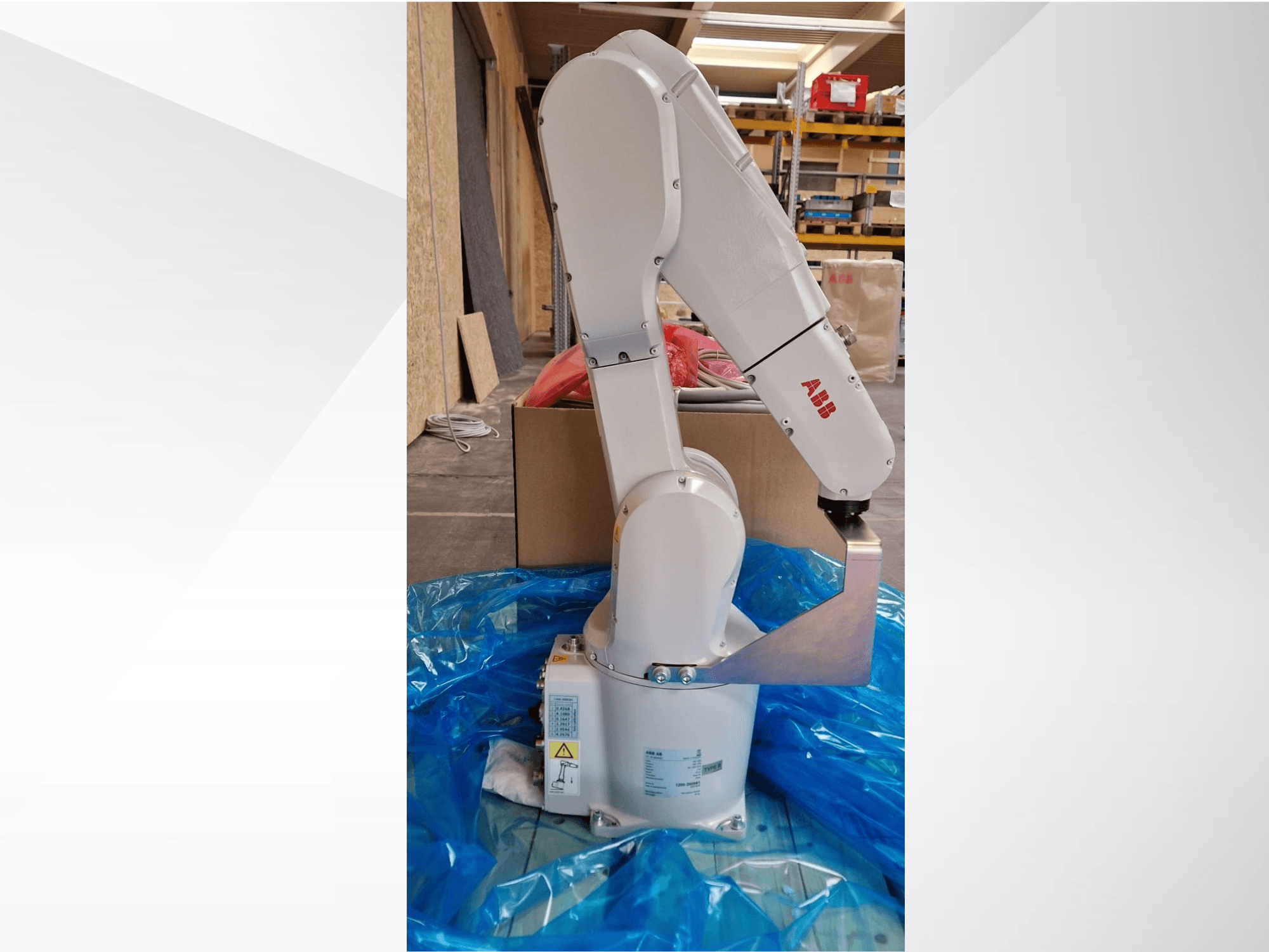 ABB robotik kol modeli, mavi muşamba üzerinde yandan görünüm, mafsallı eklemler ve metal uç efektörü sergiliyor, teknik etiketler görülebilir.