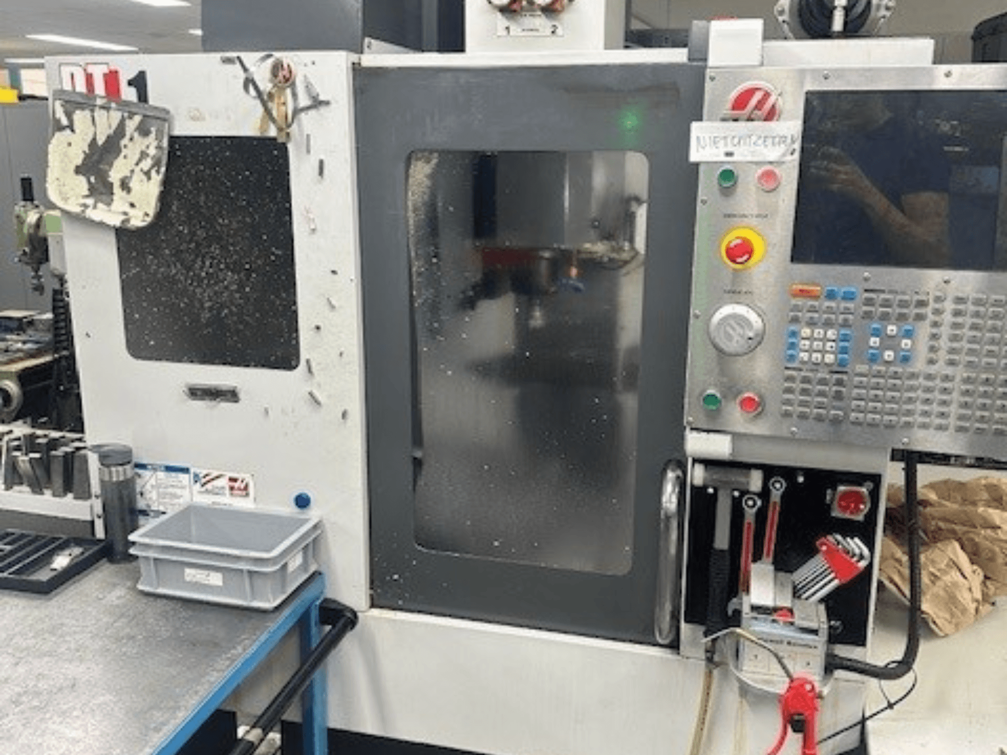 Haas DT-1 Dikey İşleme Merkezi, kontrol paneli, görünür kir ve tezgah üzerindeki takım tepsisi ile önden görünüm.