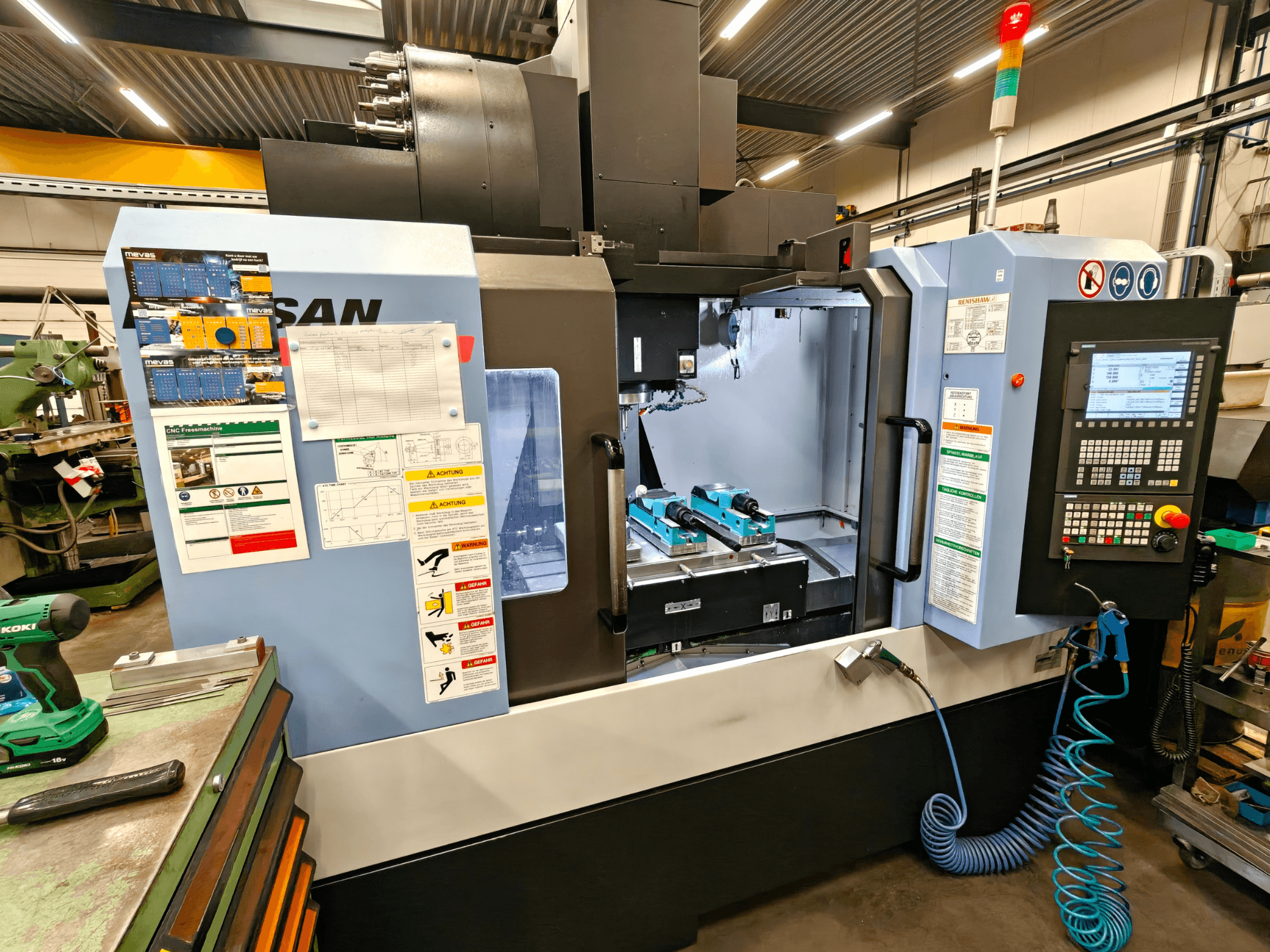 DOOSAN DNM 400 II dik işleme merkezi, atölyede, kumandalar, takım tutucular ve güvenlik işaretleri, önden görünüm.