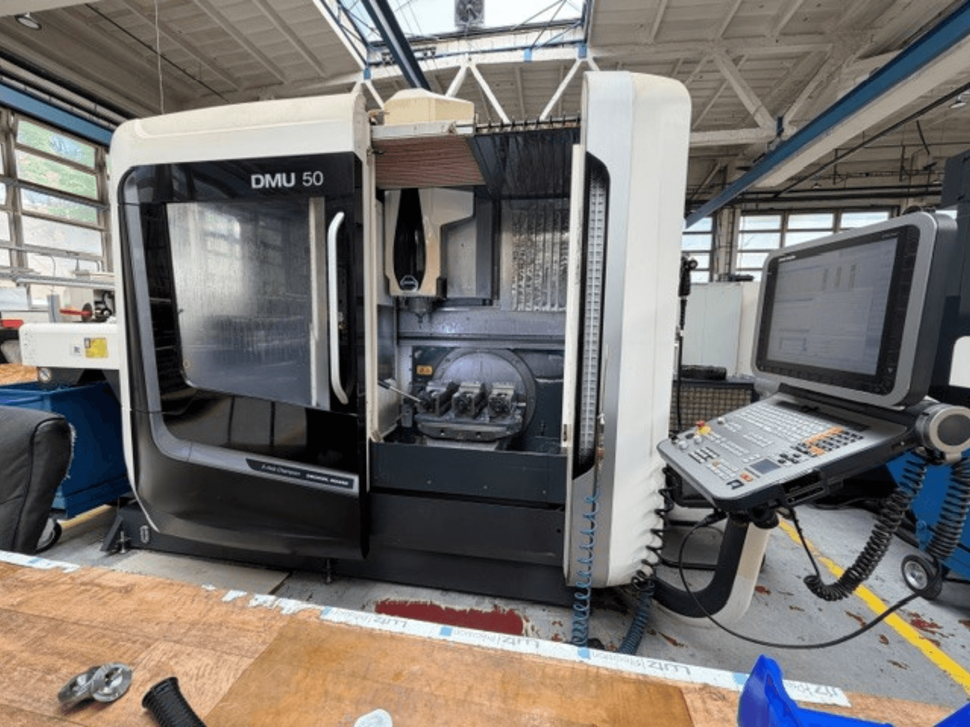 DMG MORI DMU 50 3. nesil dikey işleme merkezi, önden görünüşüyle; kapısı açık, CNC kontrol paneli görünür ve içindeki çalışma alanı.